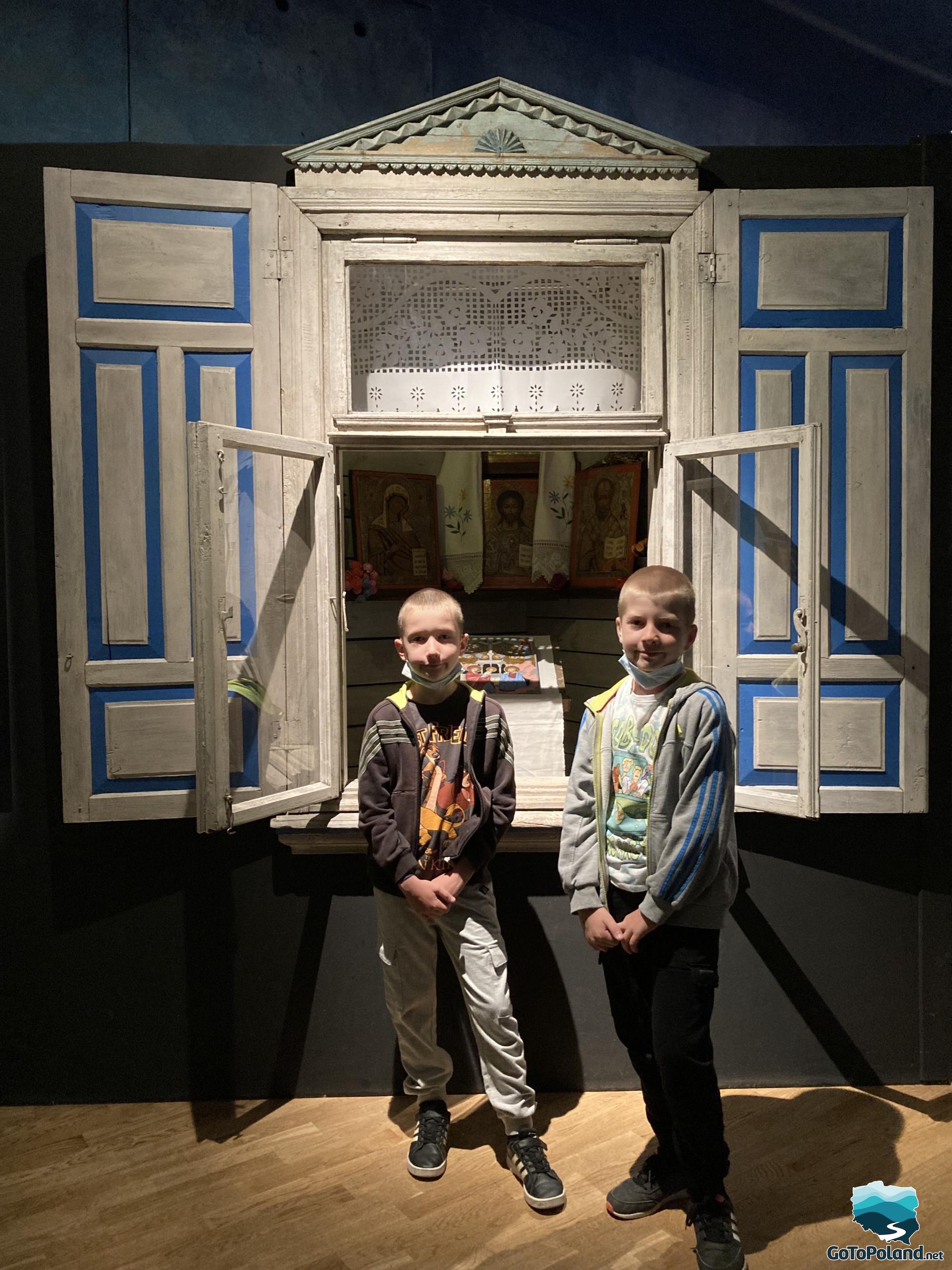 two boys are standing in front of an old wooden window, inside there is a stylized chamber with icons