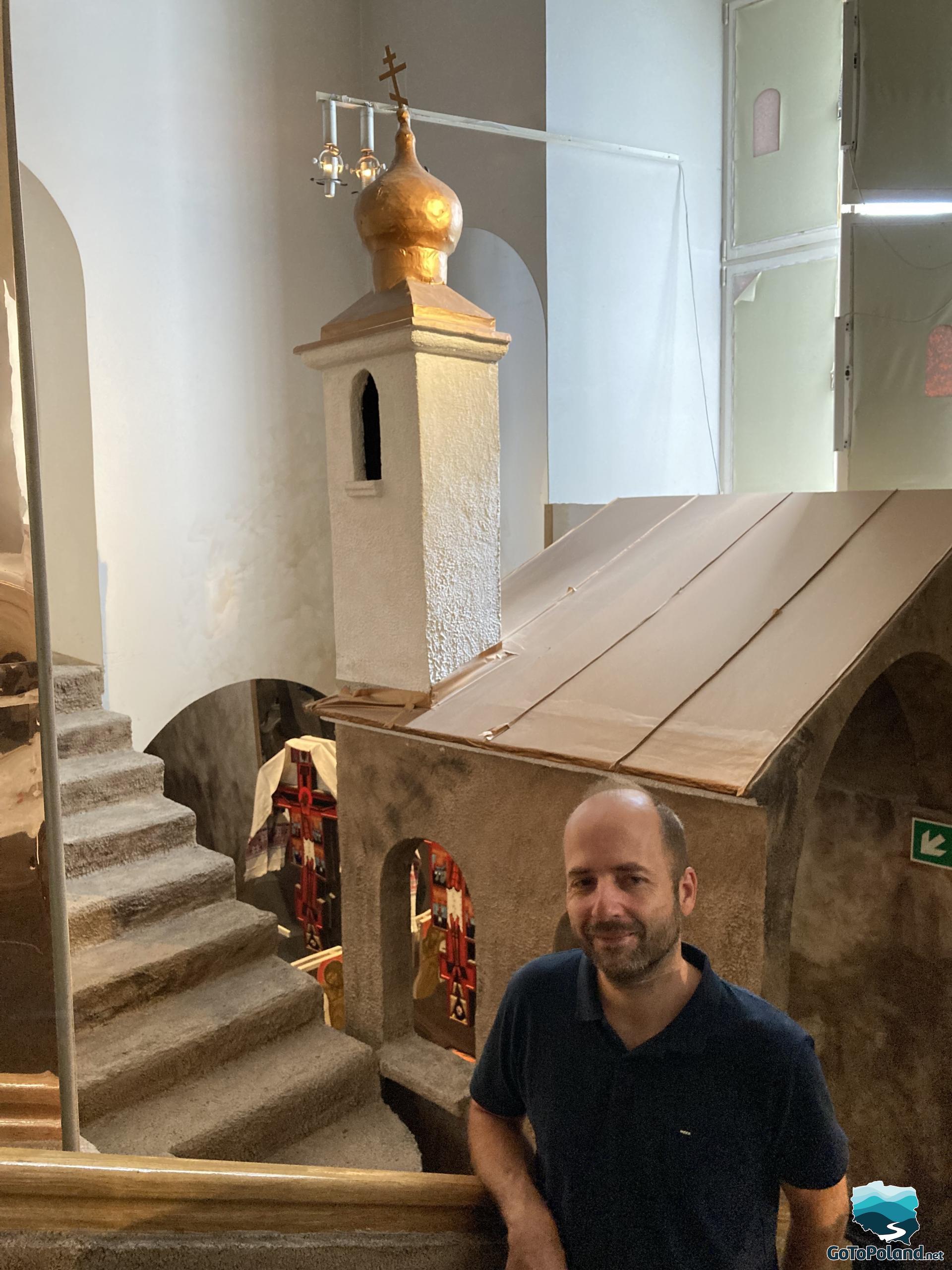 a man is standing on the stairs inside the museum, behind him an exhibition in the form of a small church