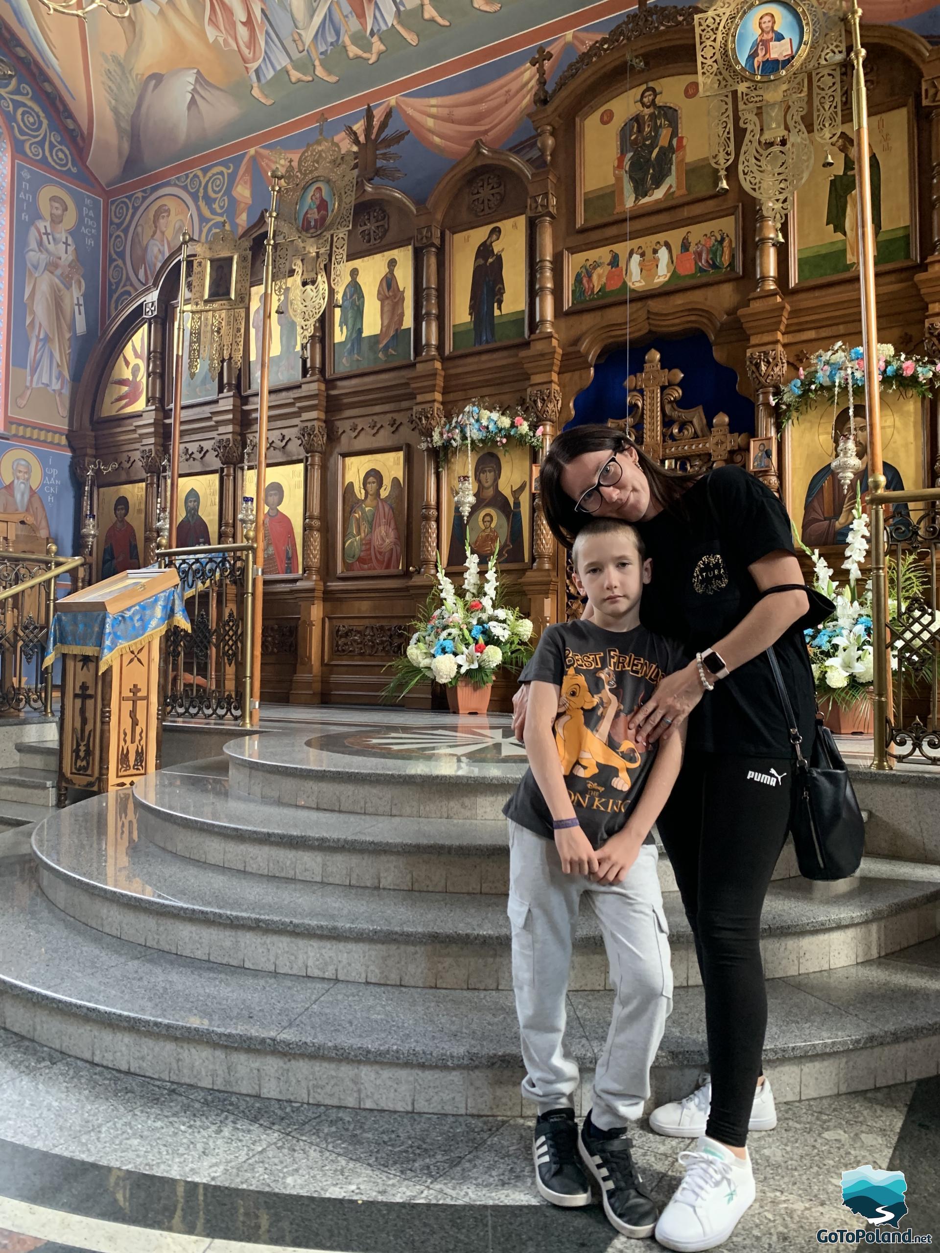a boy and a woman are standing in front of the richly decorated iconostasis