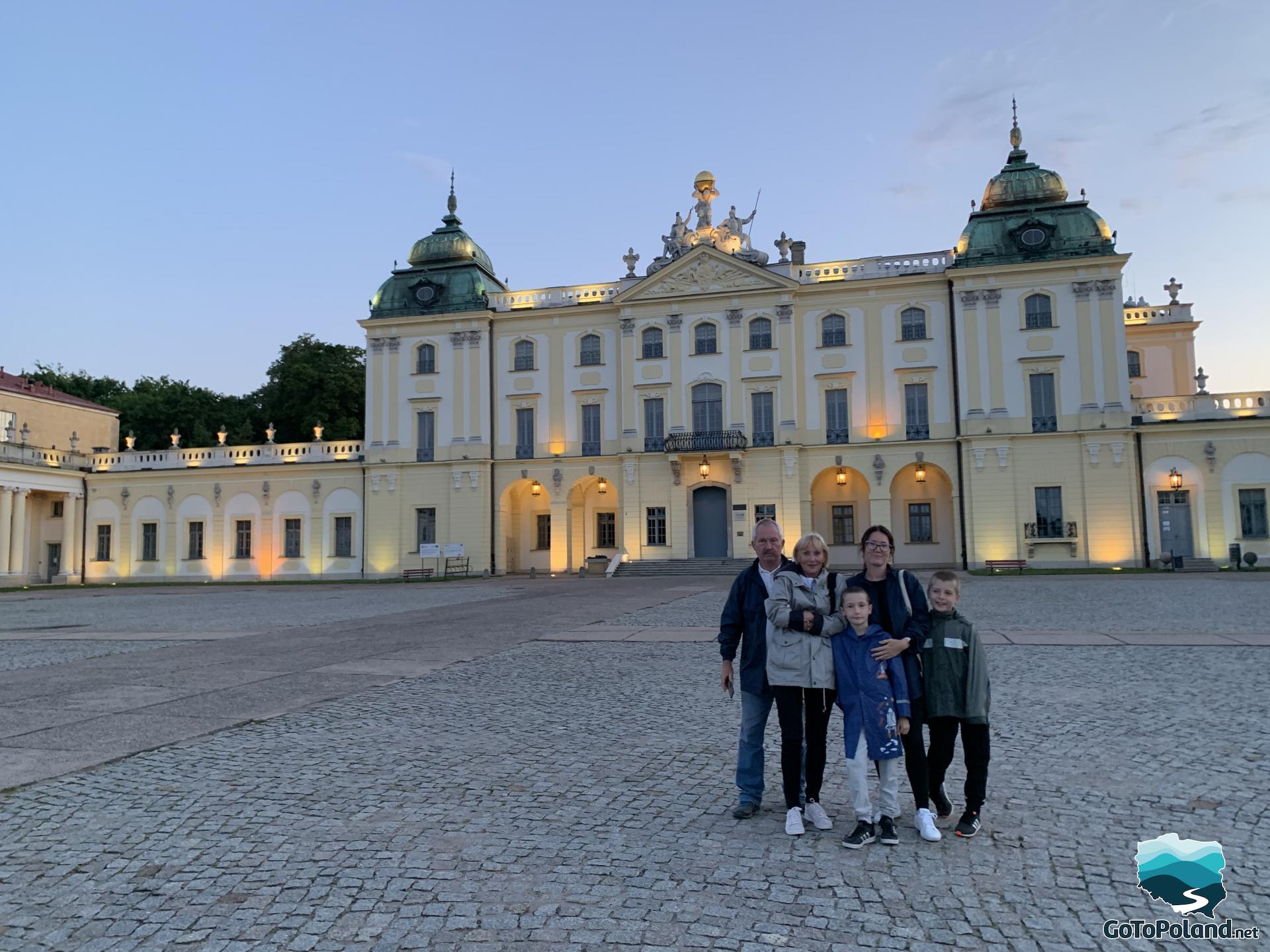 a family is standing in front of the castle, the palace is illuminated because it is already evening