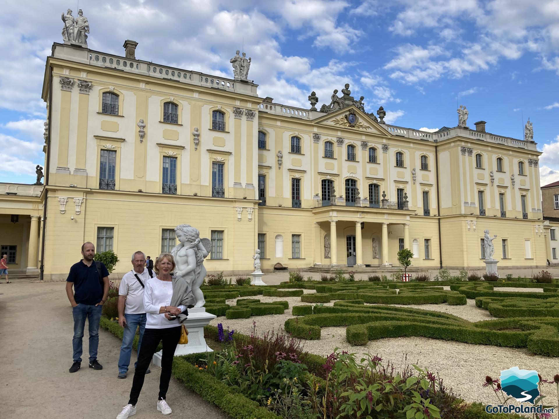 two men and a woman are standing in front of the palace, they are in the garden