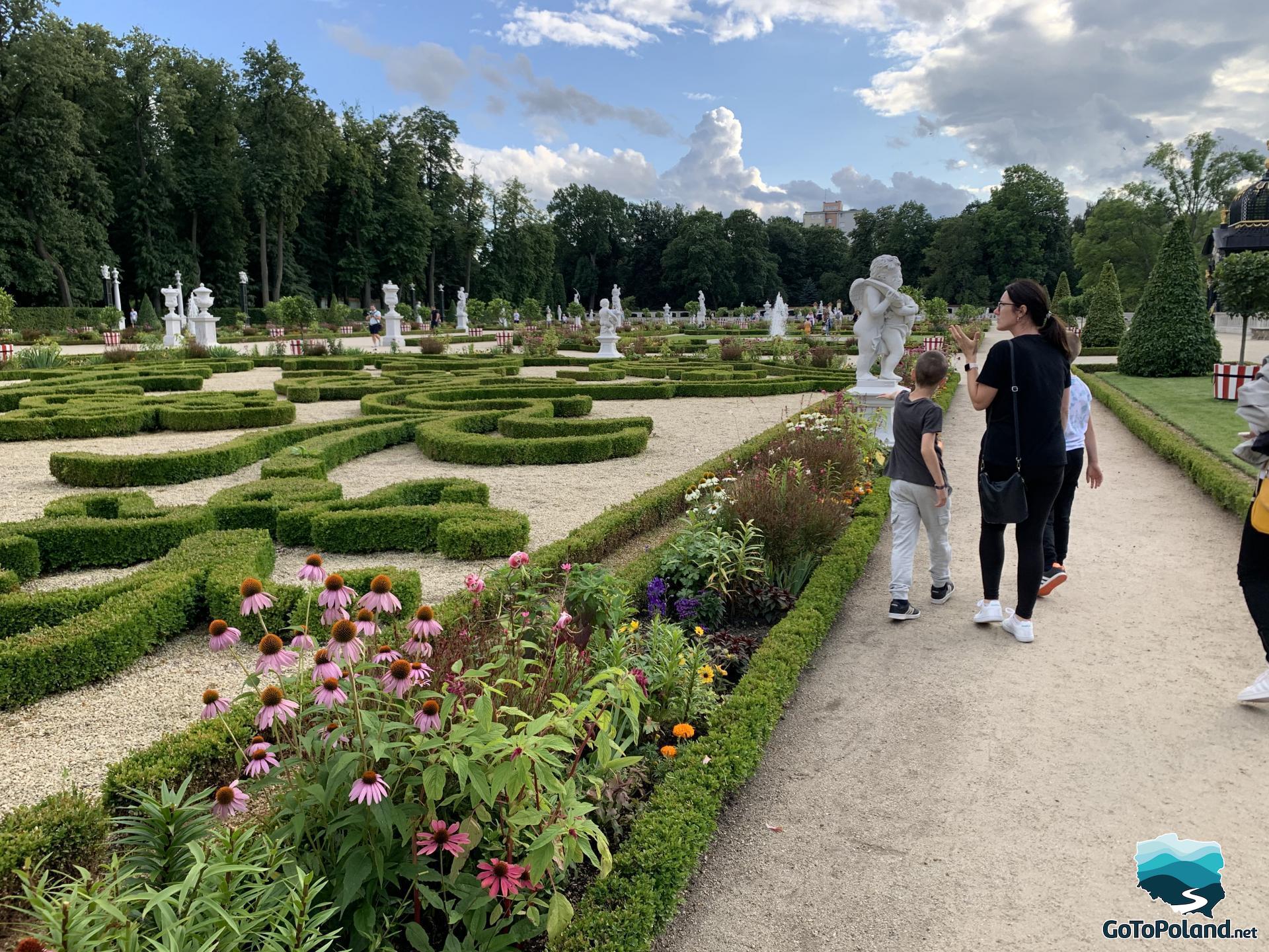 a woman and two boys are walking along the paths in the palace garden