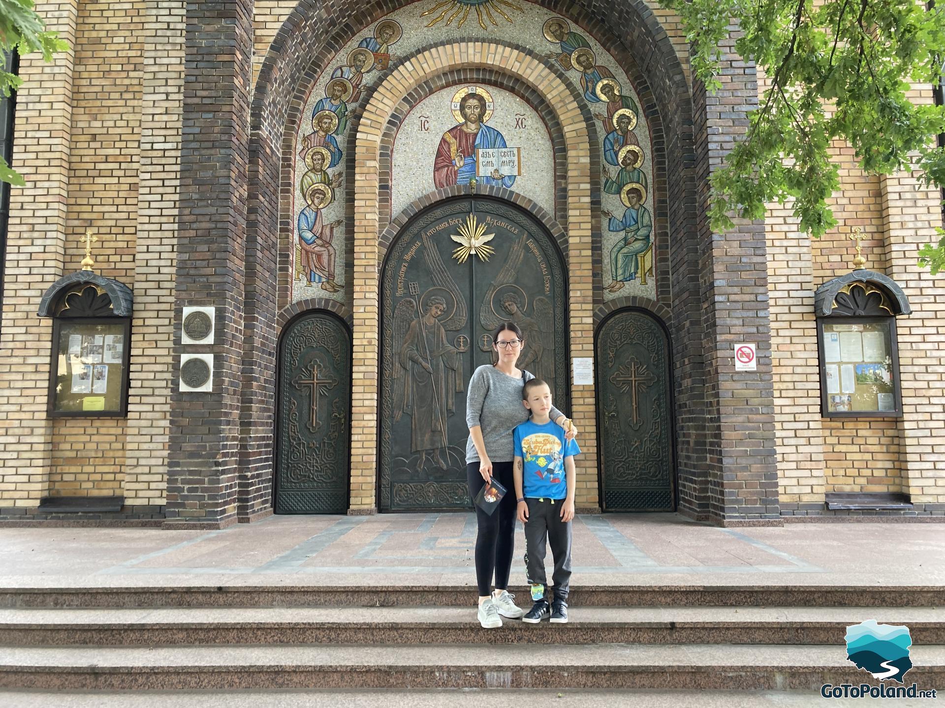 a woman and a boy are on the stairs leading to the Orthodox Church