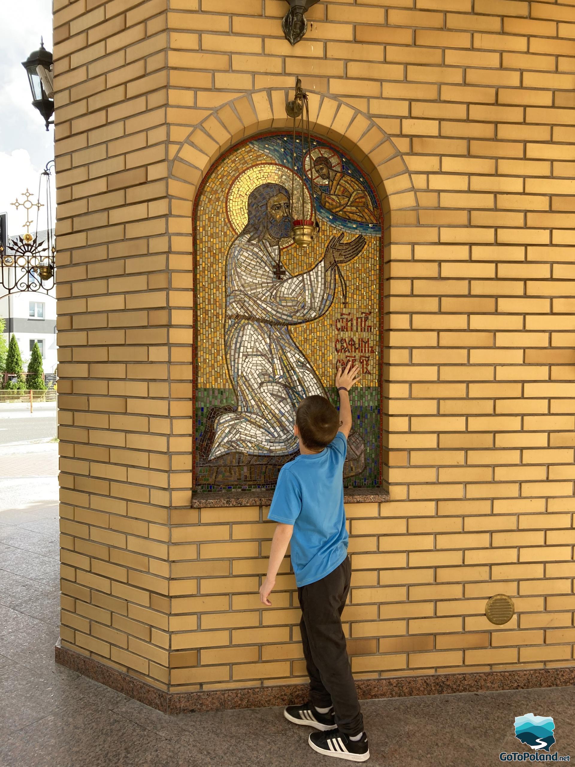 the boy is standing by the image of christ, which is placed in a rectangular pillar made of bricks