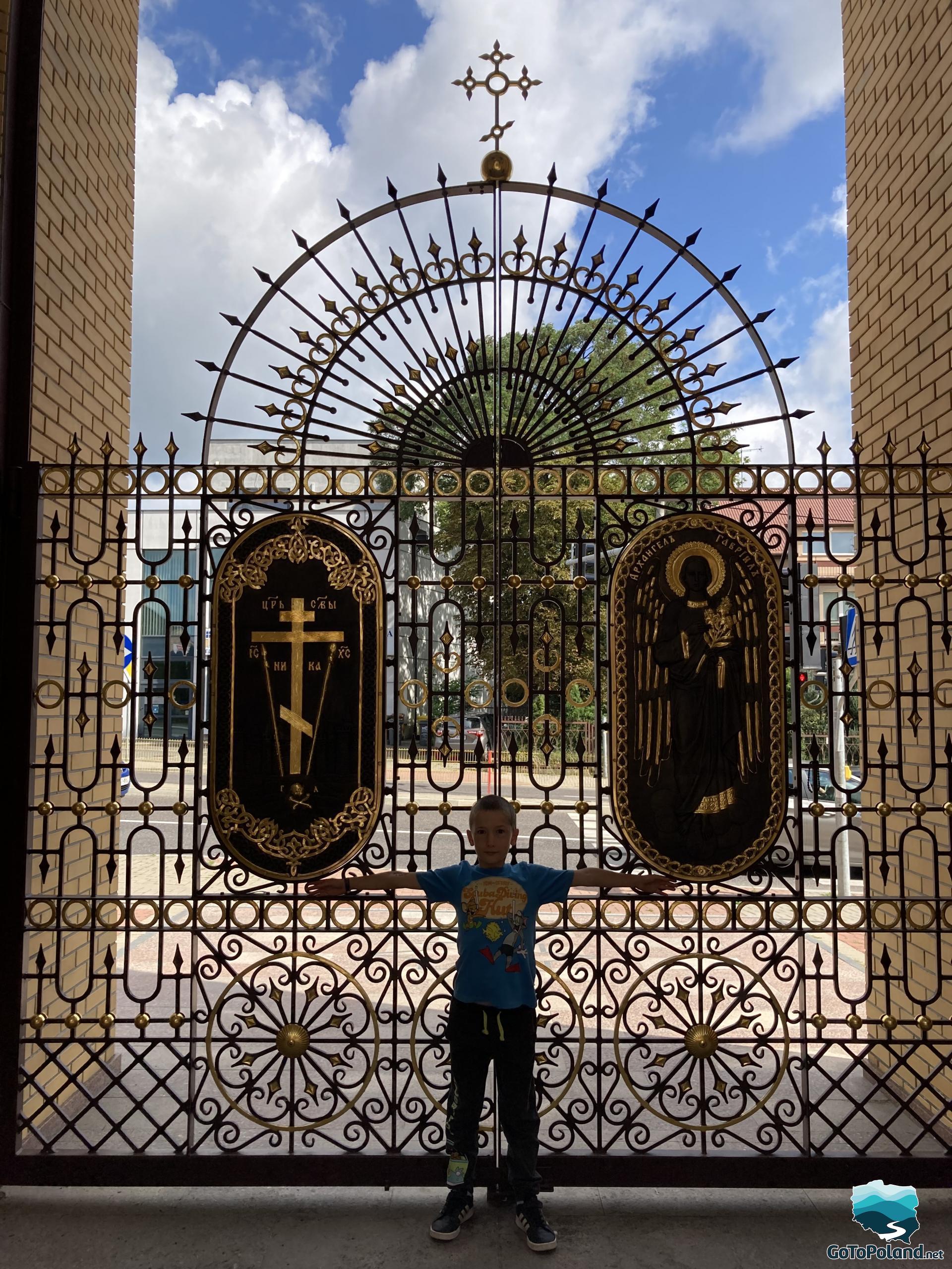 the boy is standing by the openwork gate leading to the orthodox church