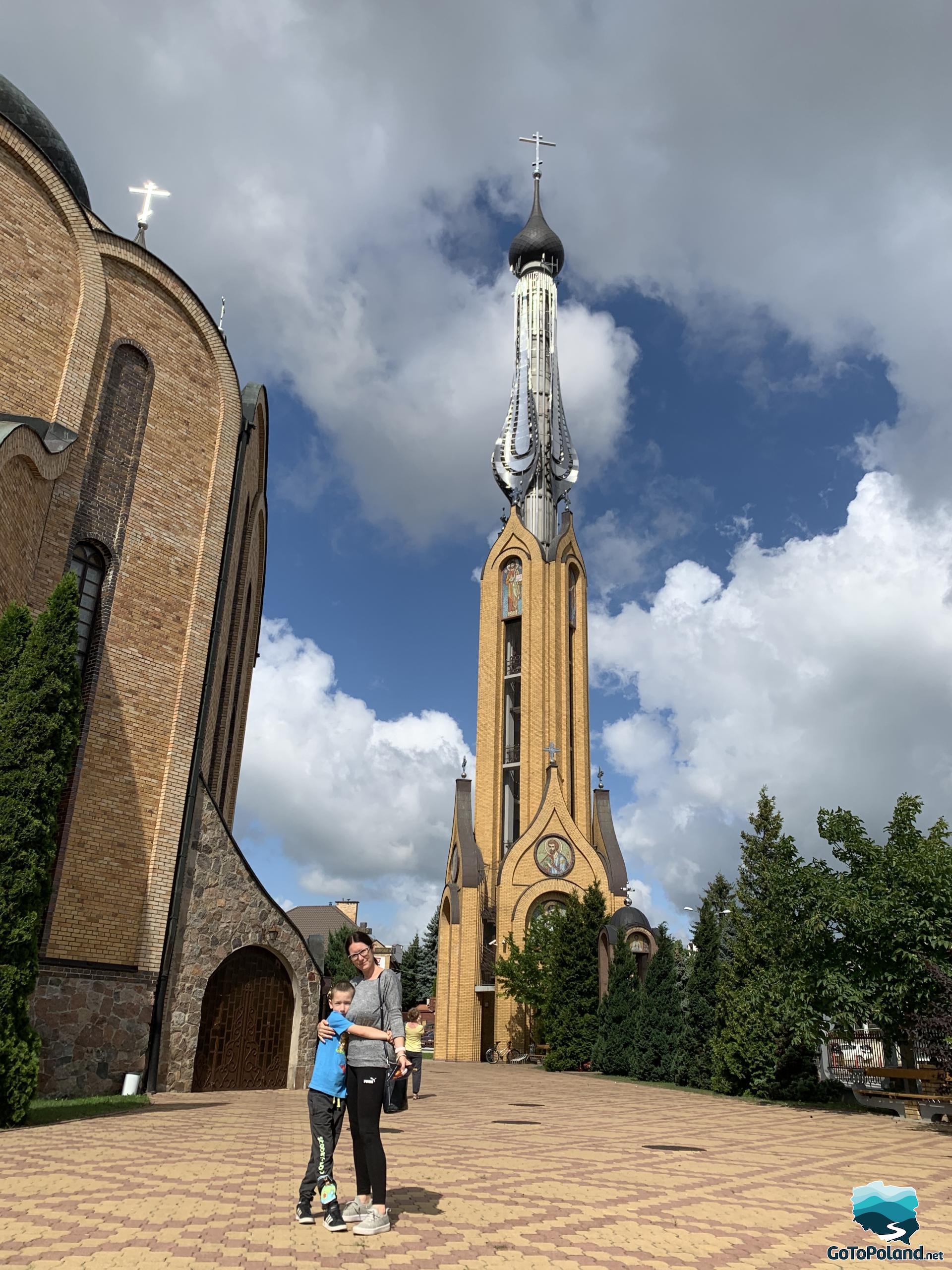 a woman and a boy are near the huge orthodox church, behind them there is a big tower