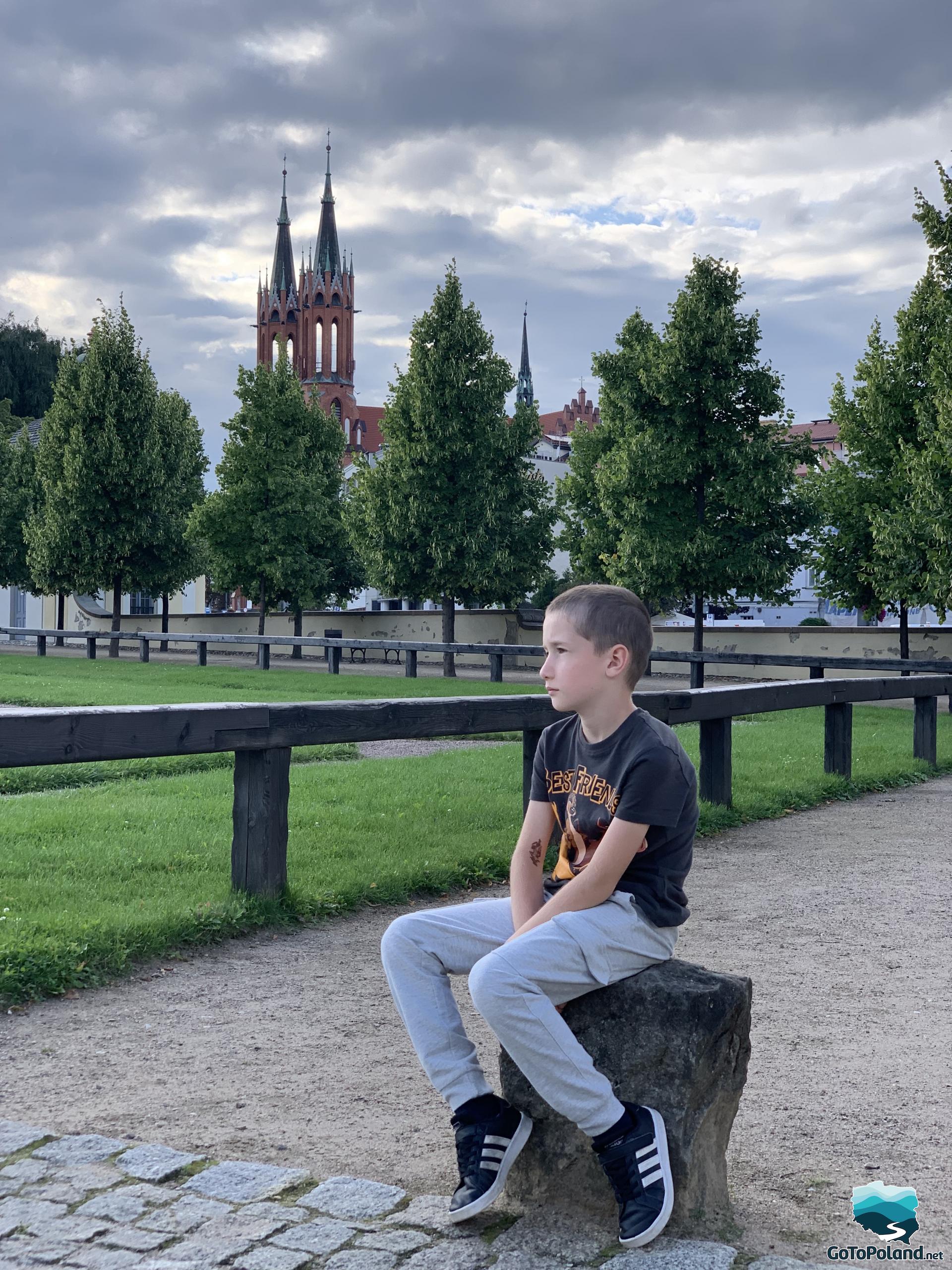 a boy is sitting on a stone, in the background trees and a church