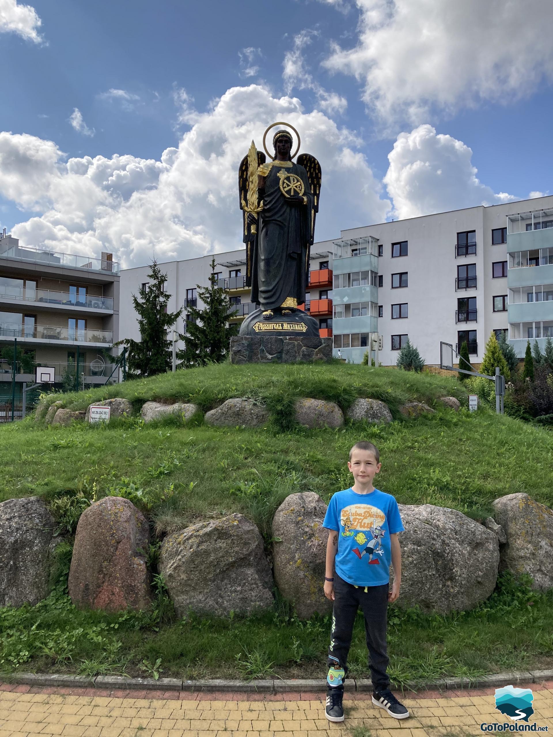 a boy is standing in front of a statue of an angel with wings