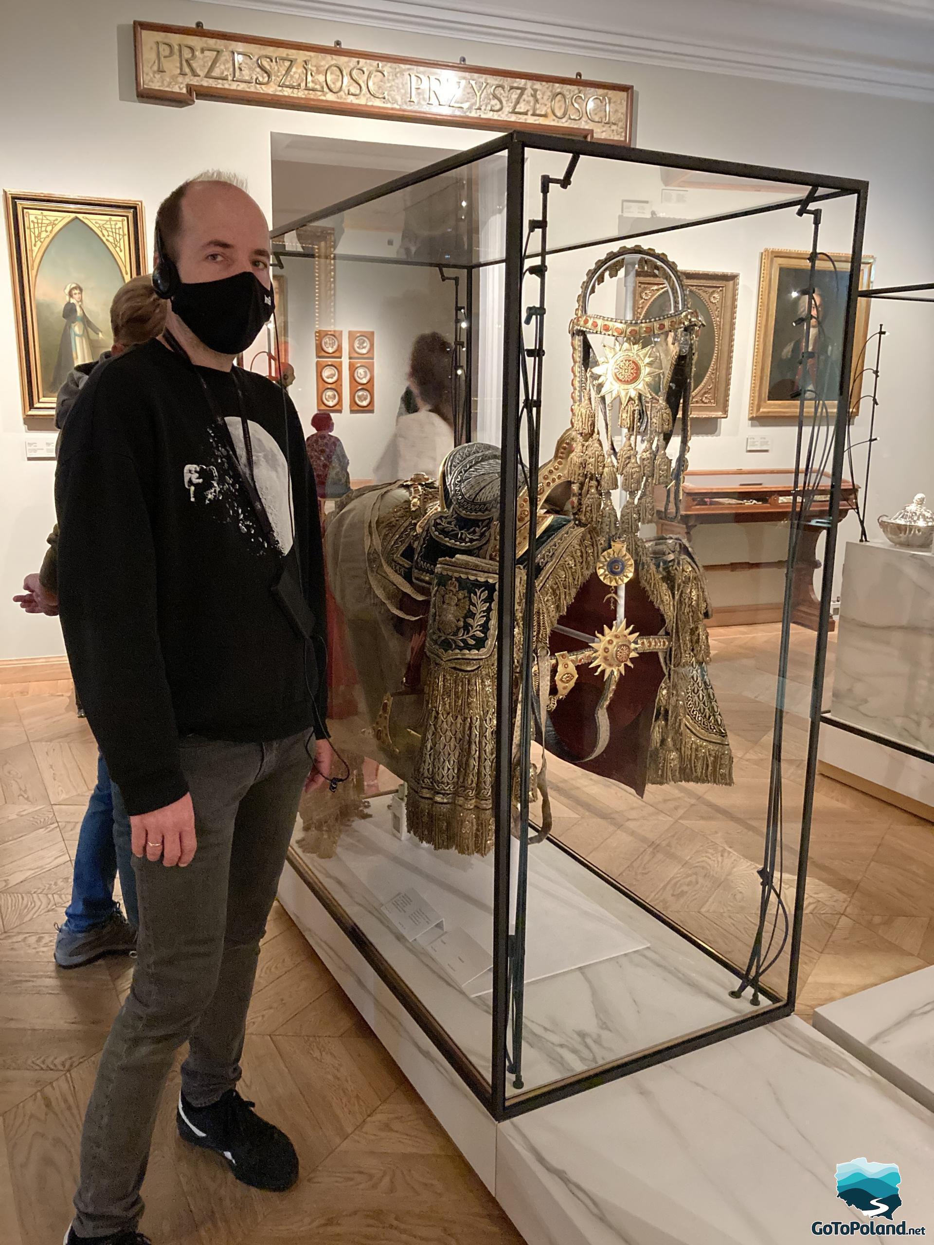 A man is standing next to the exhibit. This is a very decorative saddle maybe from the 16th or 17th century placed behind glass