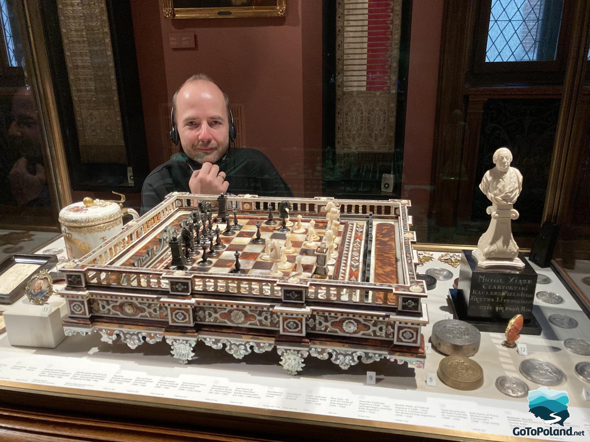 A man is next to the old chess. There are also old coins