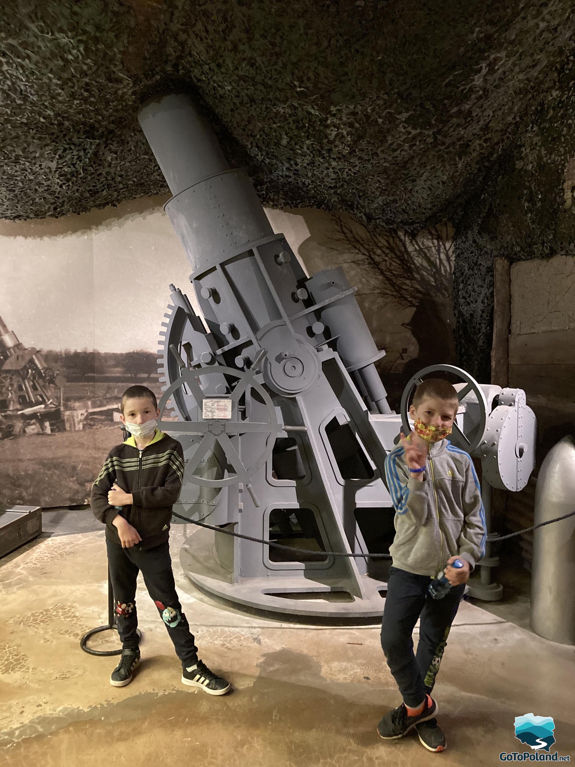 A large, grey cannon and two boys in front of it.
