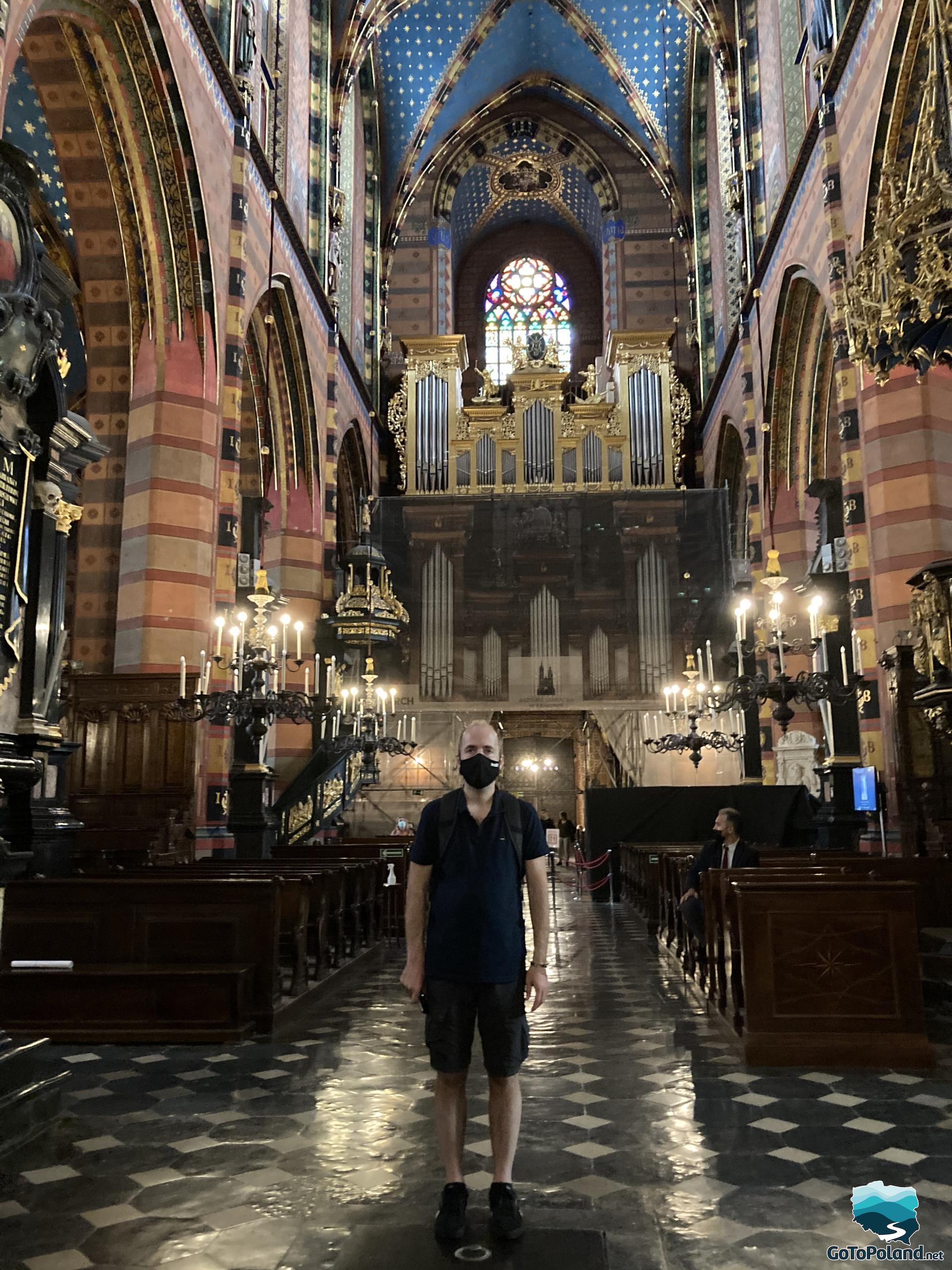a man is standing inside the church, behind him there is the organ and rows of pews
