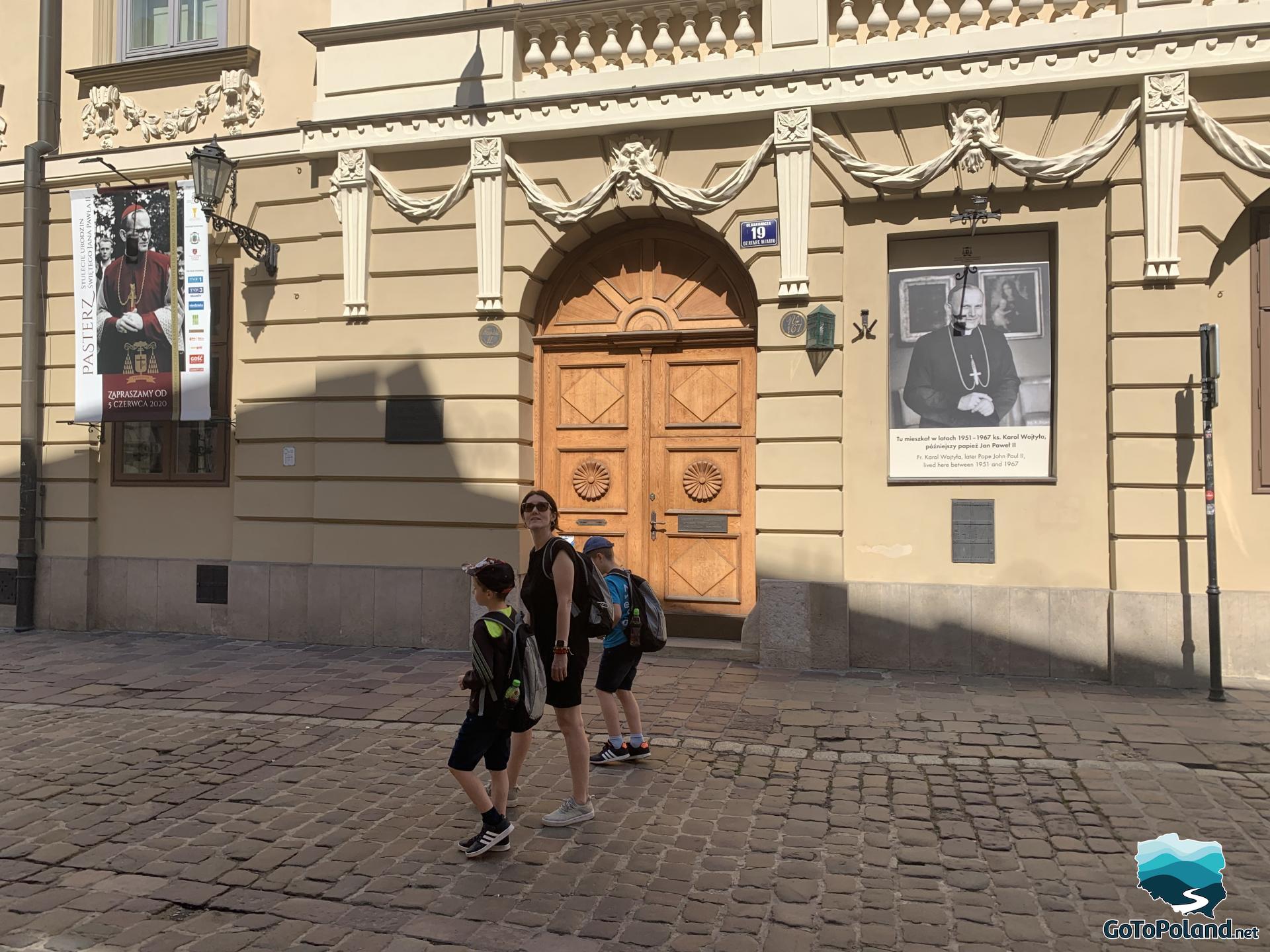 two children and a woman are walking along the building where Pope John Paul II lived