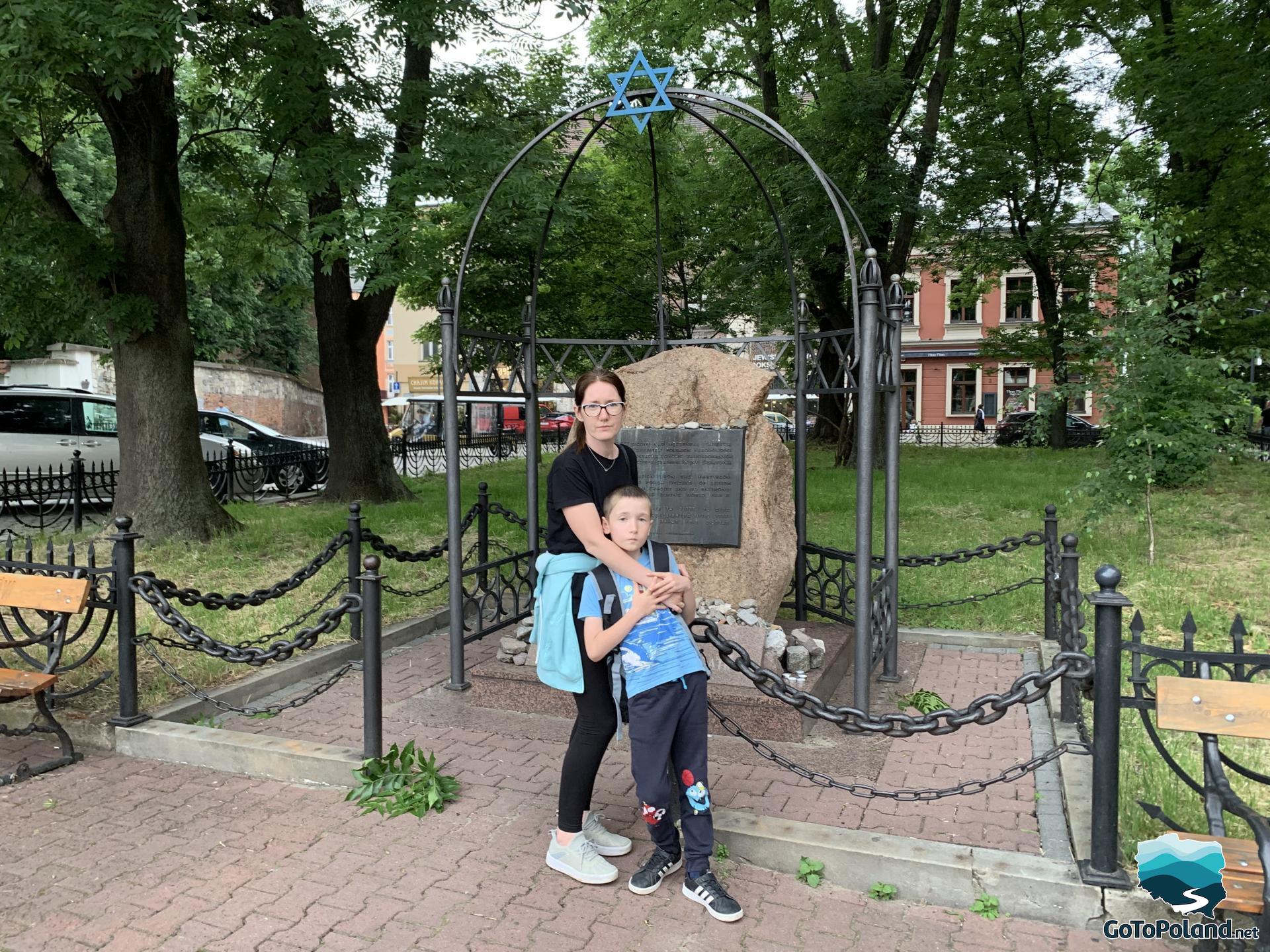 a woman and two children are in front of a stone which is a monument in honor of Jews
