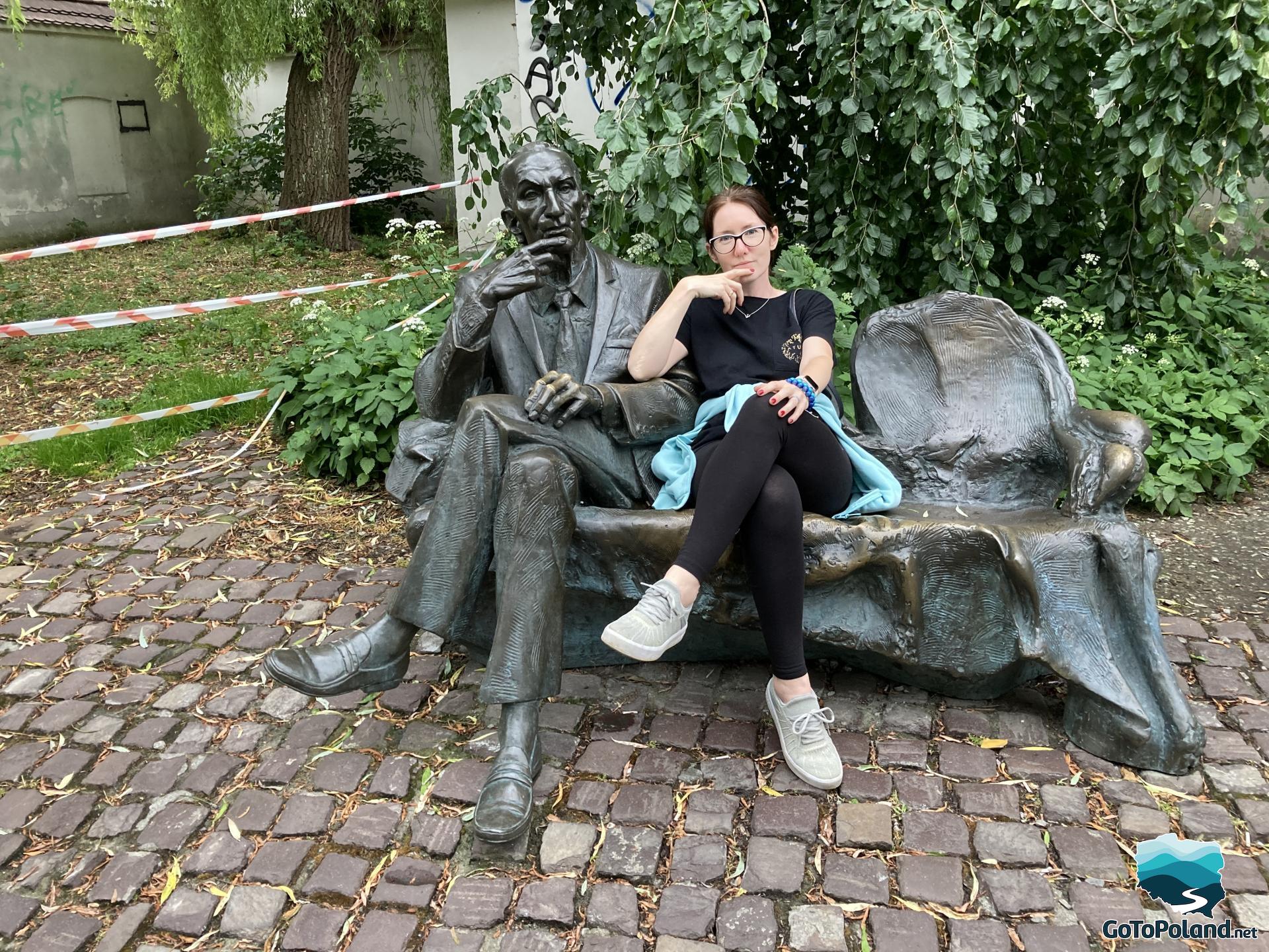 a woman is sitting on a bench which is a fragment of sculpture joined with a sculptured man