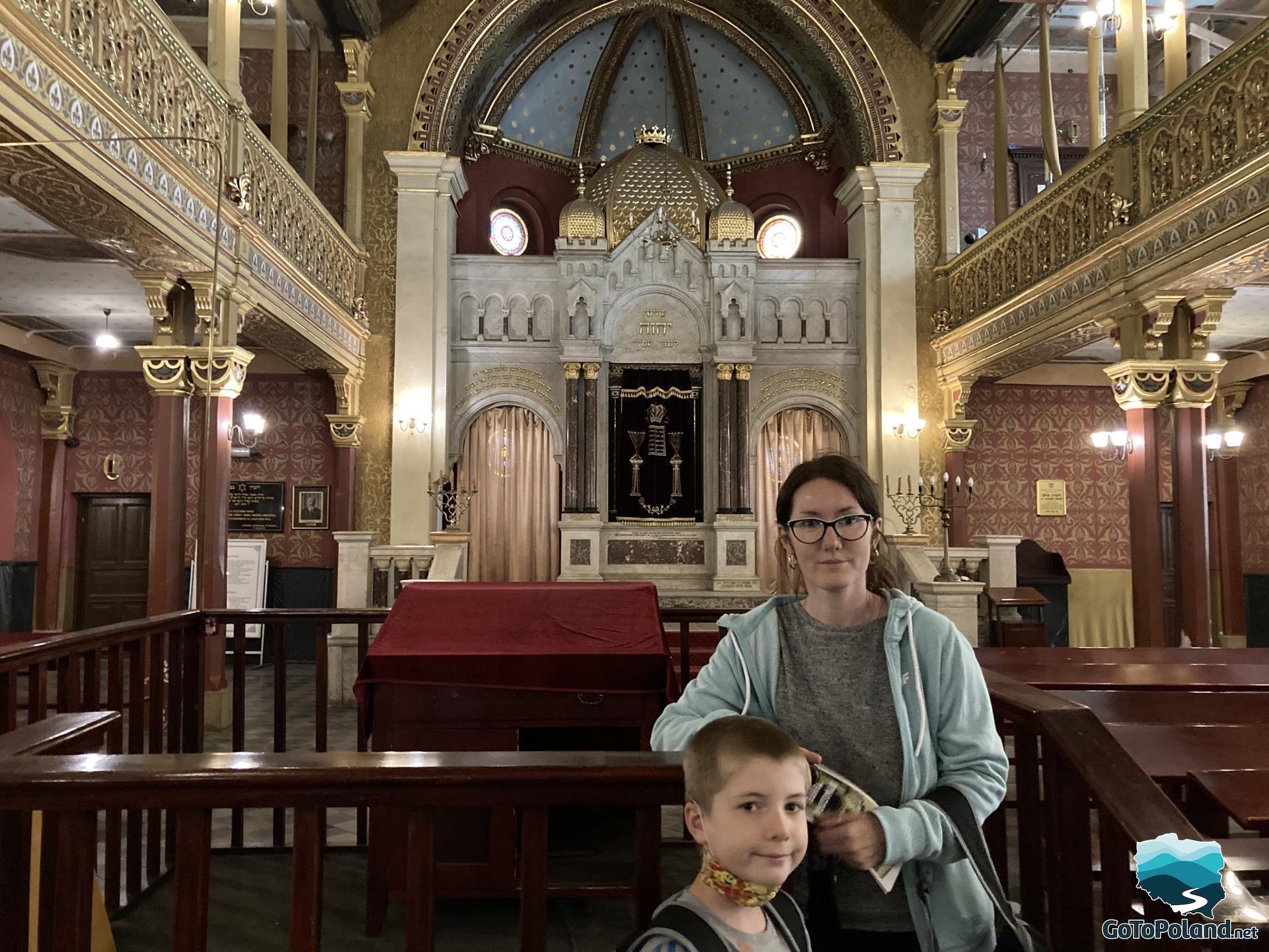 a boy and a woman are in a synagogue, behind them there is an altar cabinet used to store the Torah scrolls