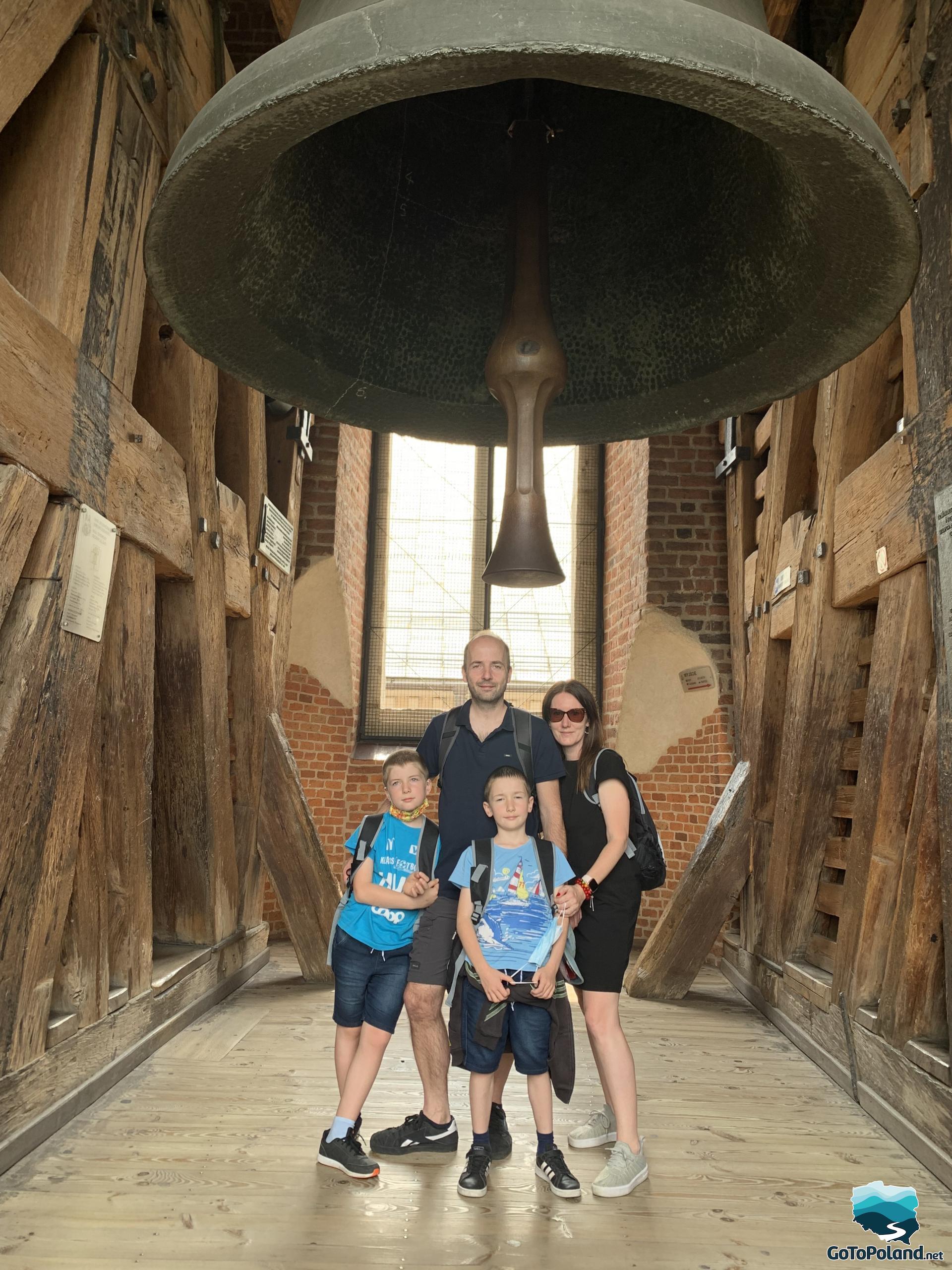a family is standing under a huge bell