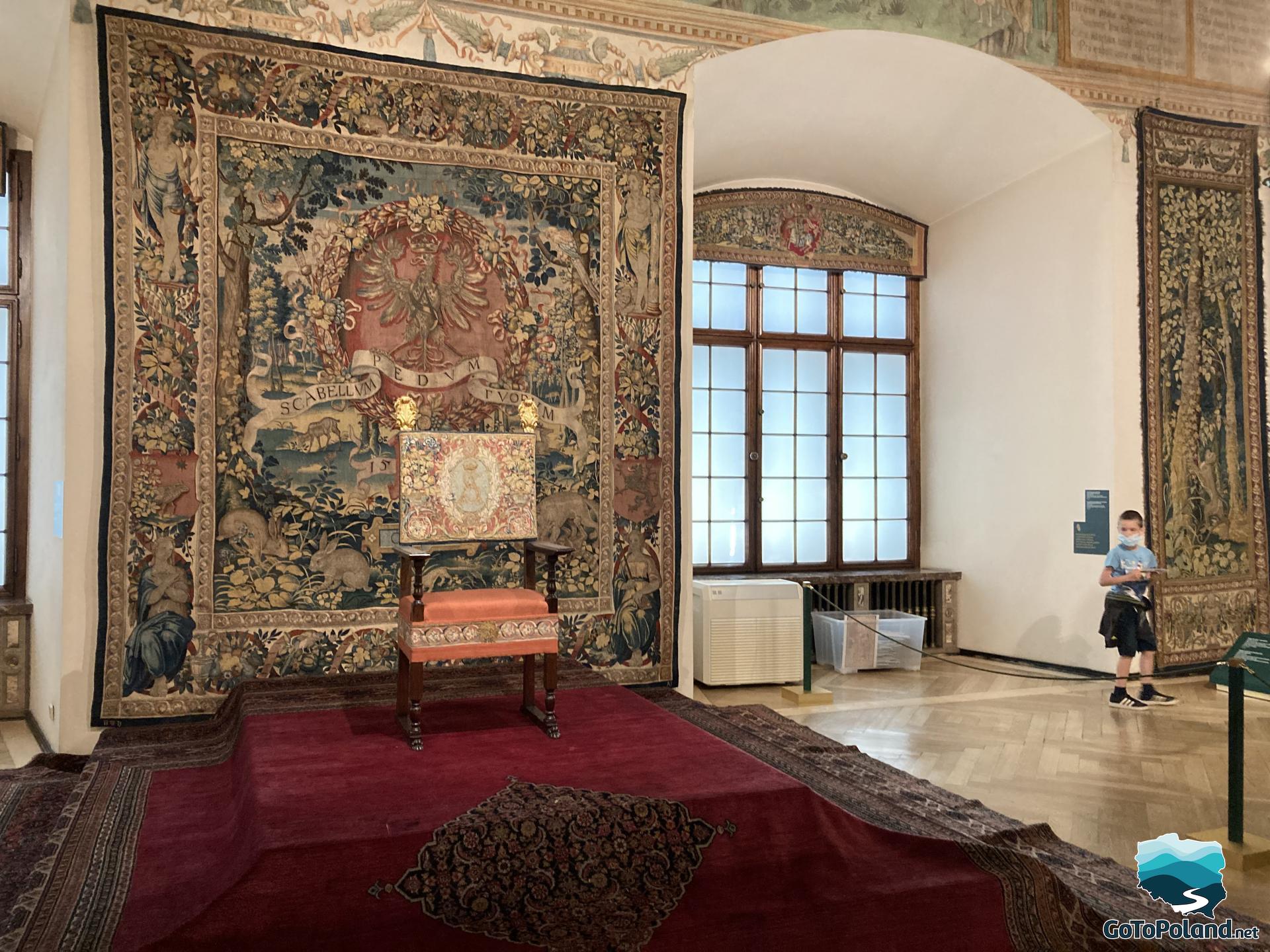 the boy is standing in the chamber, there are large windows, in the middle there is a throne chair and a tapestry is hung behind the chair
