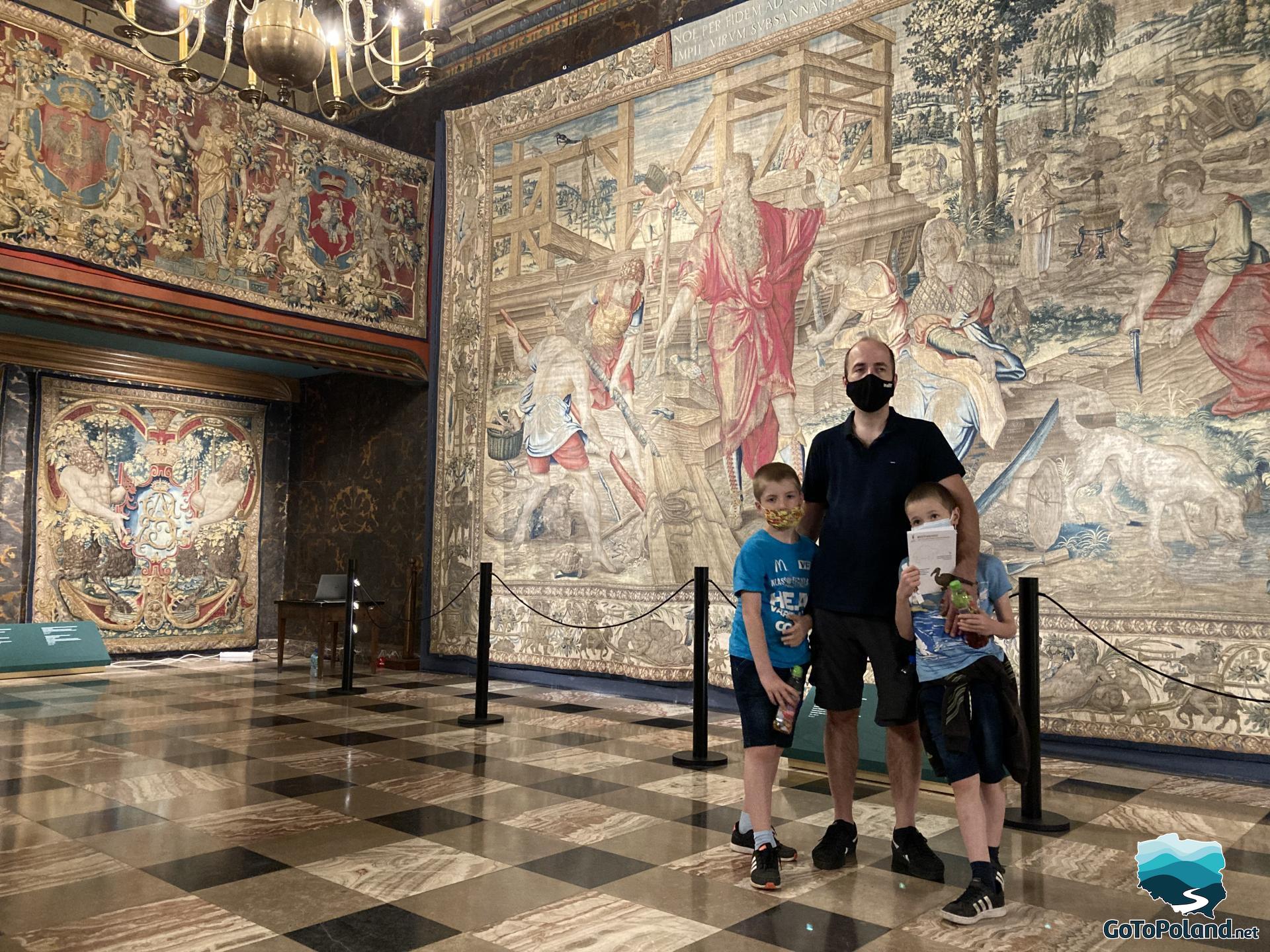 a man with two kids is standing in the middle of the hall with tapestries