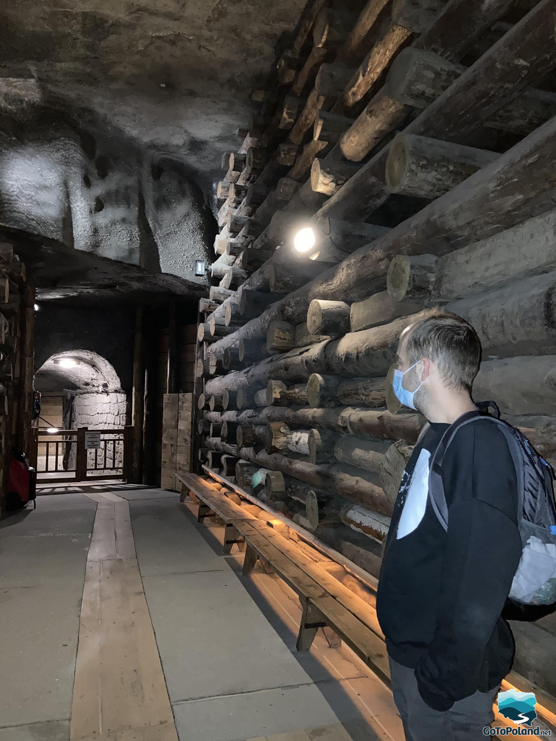 a man is standing in the corridor, the walls are made of salt, the wall on the right is reinforced with thick beams of wood