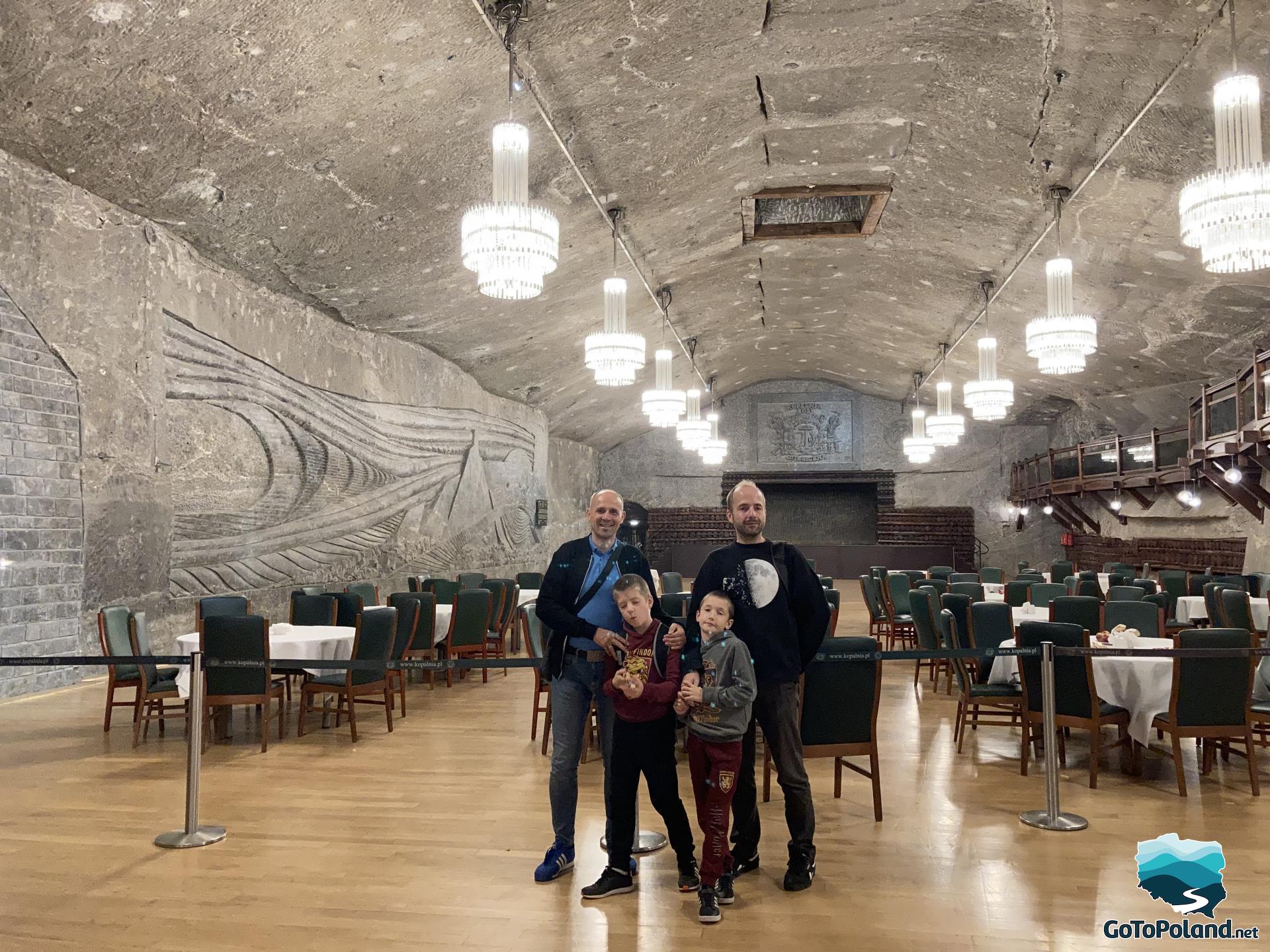 two men and two boys are in a salt mine restaurant, behind them are tables and chairs, the walls and ceiling are made of salt