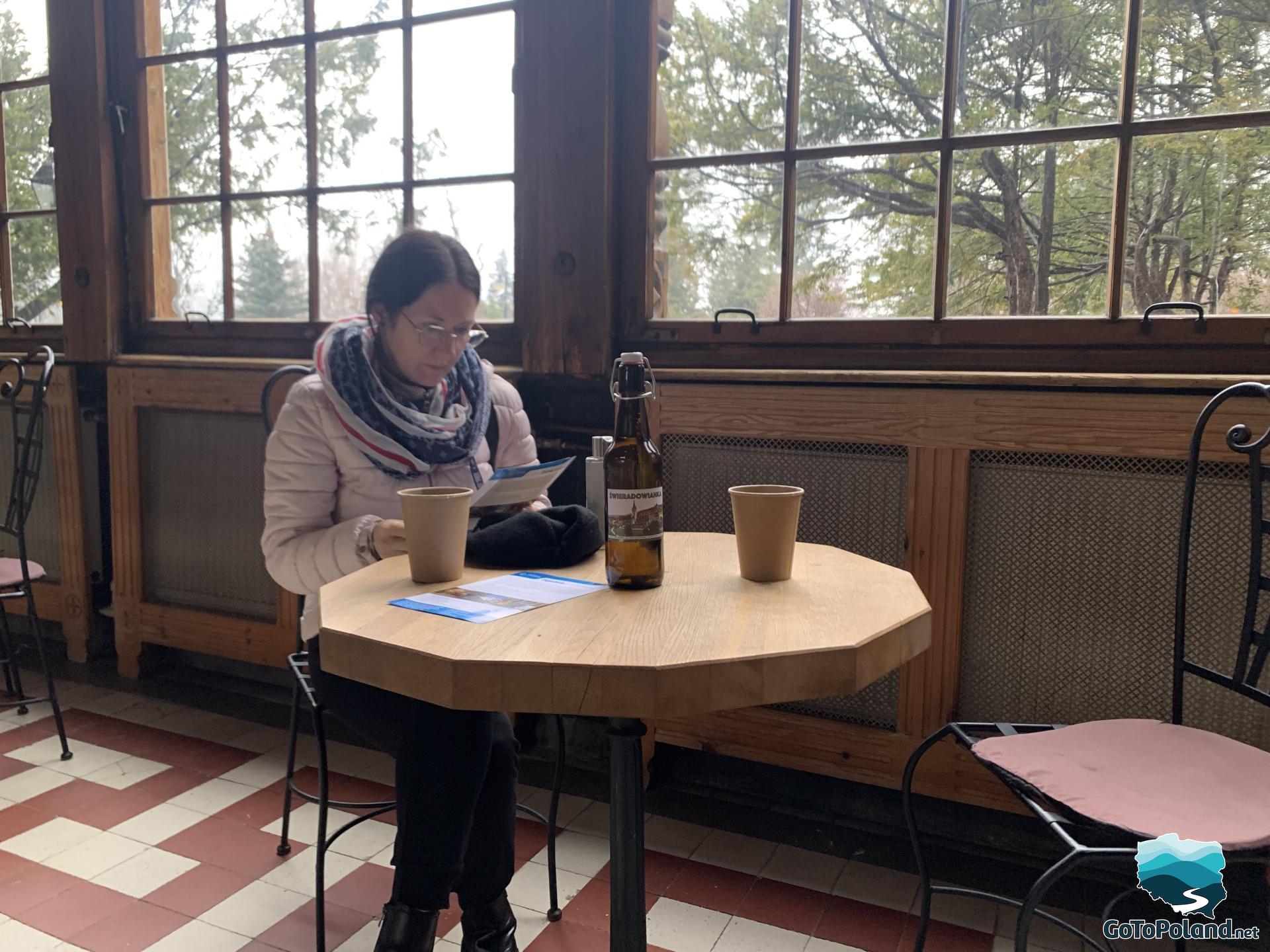 a woman is sitting at the table looking at some brochure, on the table is a bottle with healthy radon water