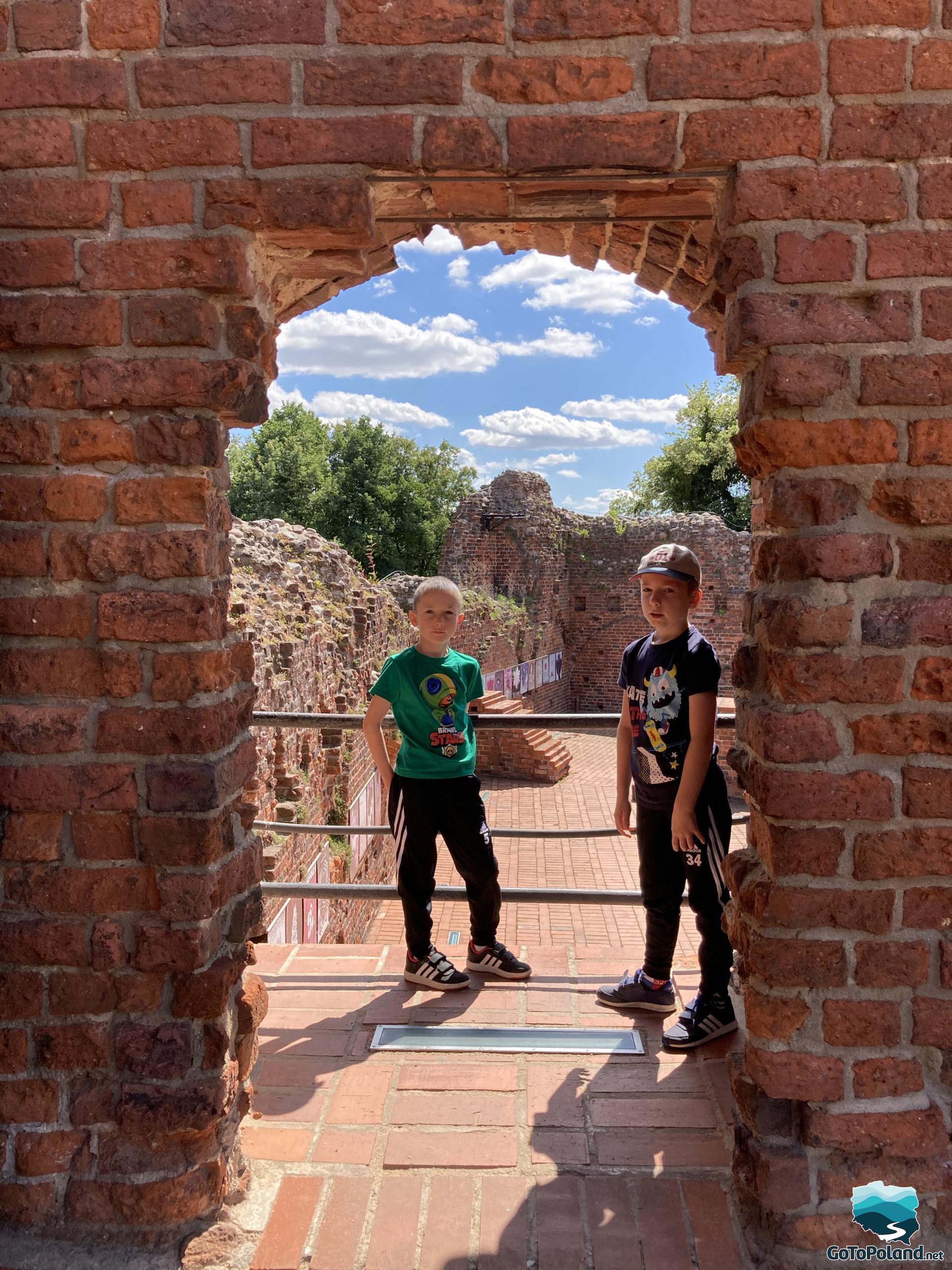 two children are standing in the entrance to the ruins of a former red brick castle