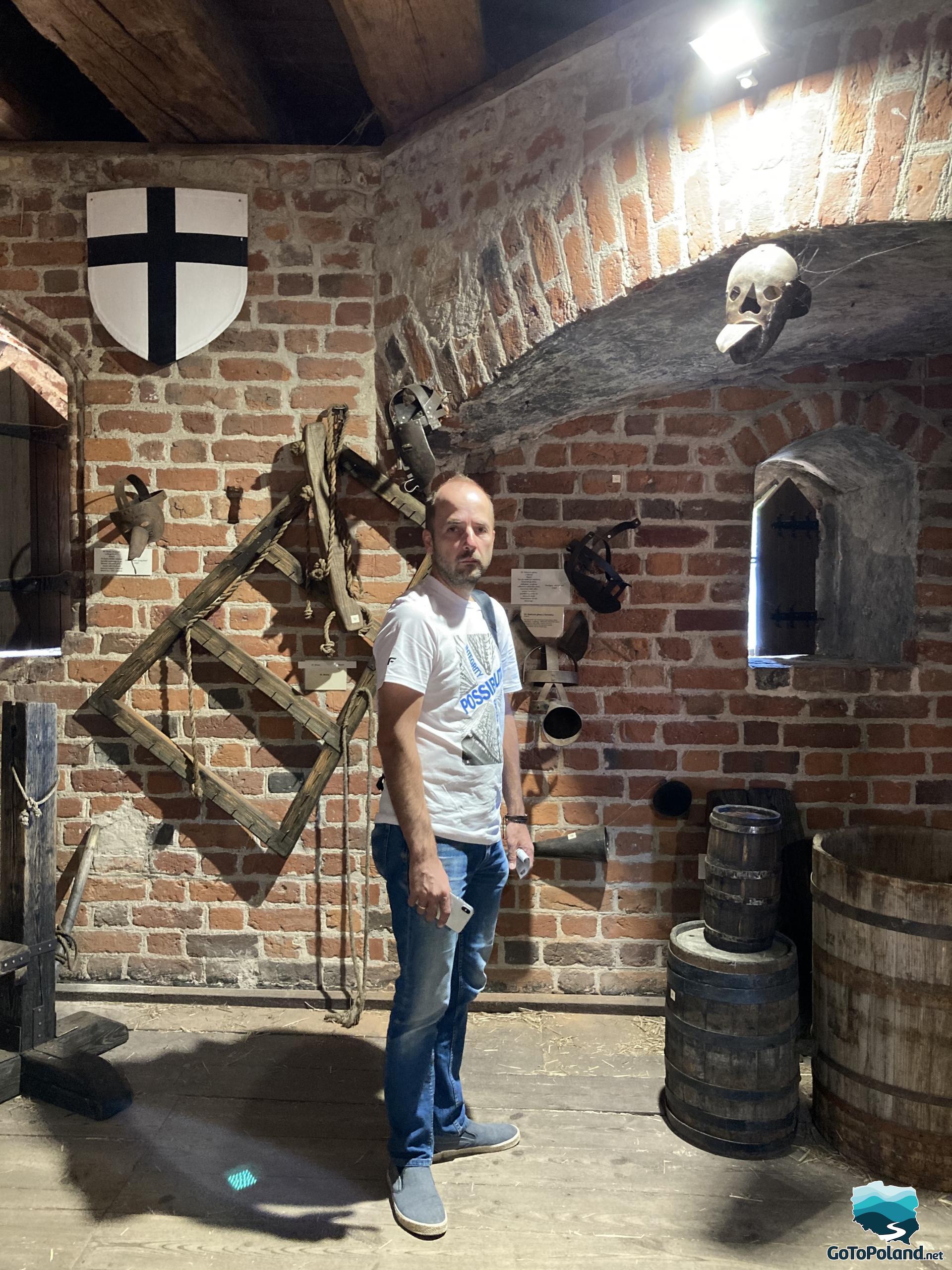 a man standing in a room in a former castle, the room is filled with old instruments of torture