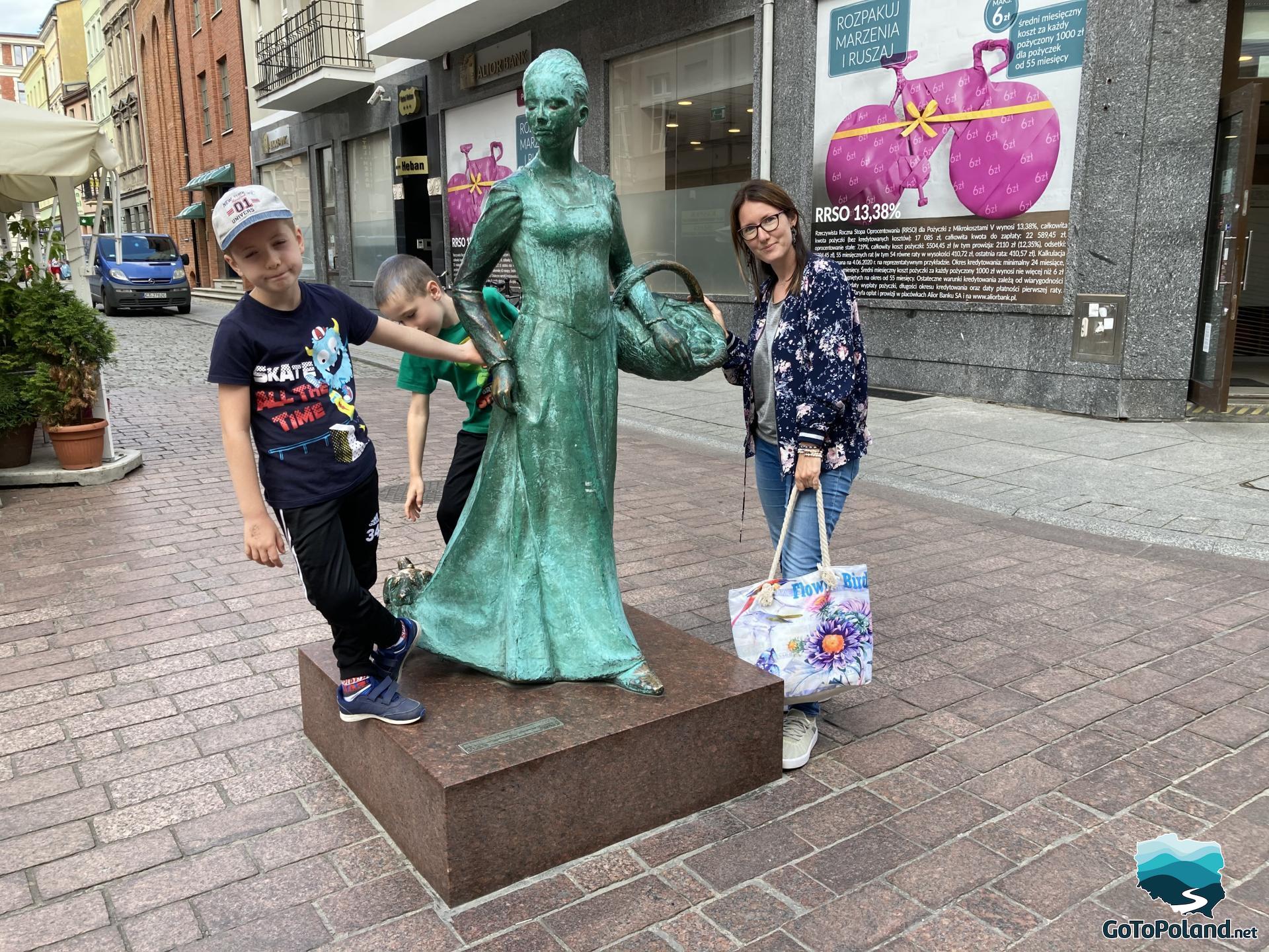 a woman and two children are standing next to a green woman statue 