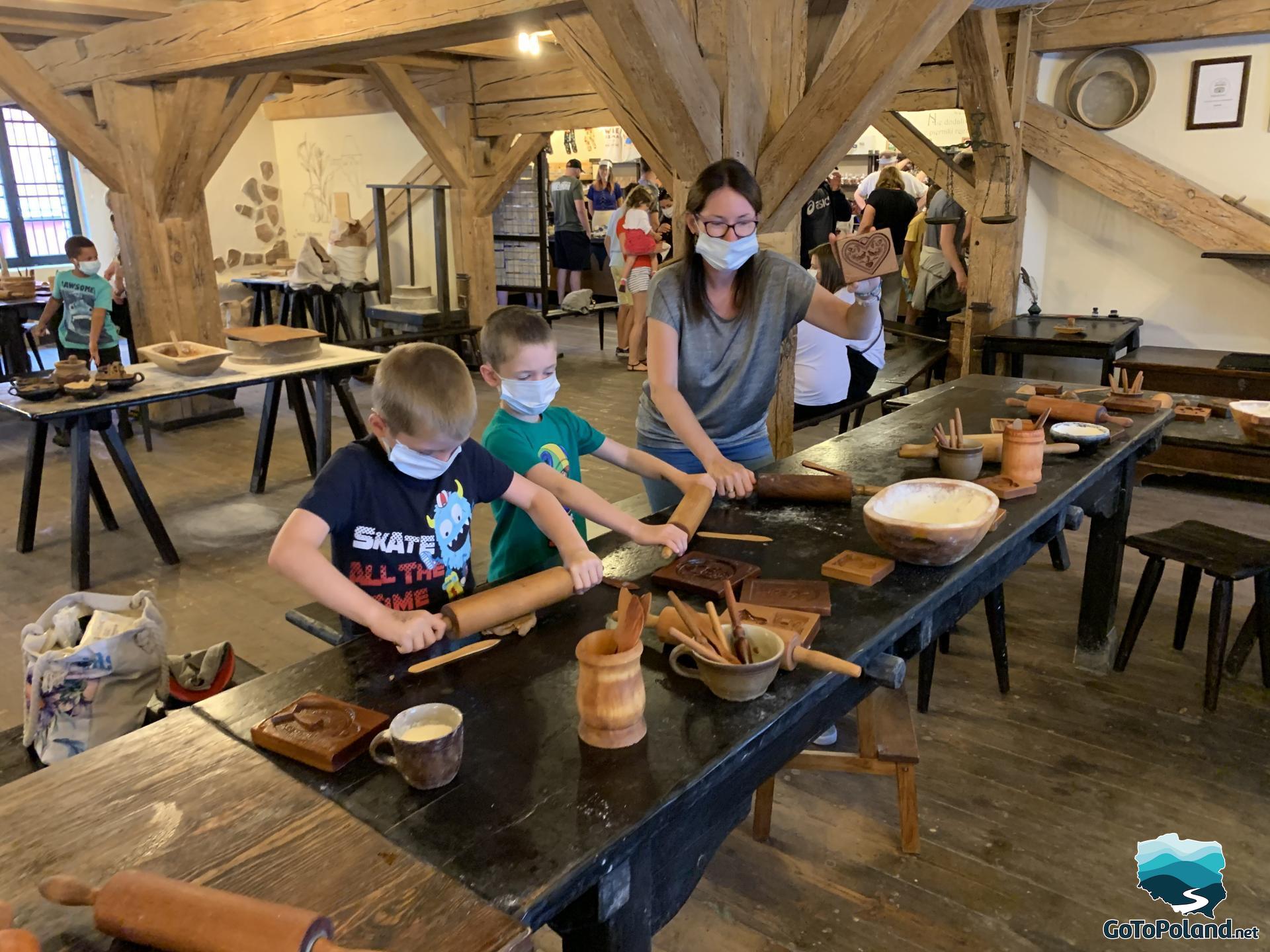 a woman and two children are in a room where they participate in gingerbread baking, they have gingerbread dough, rolling pins and various molds on the table