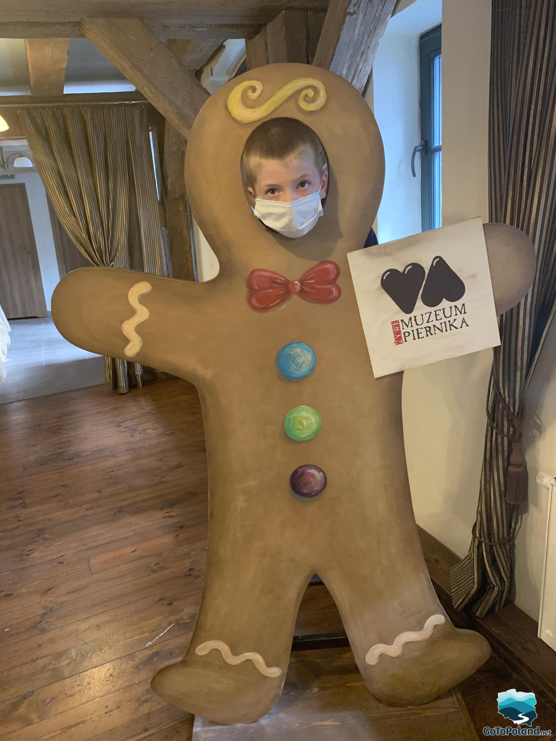 the boy is standing behind a gingerbread man made of cardboard and sticking his head out for a photo
