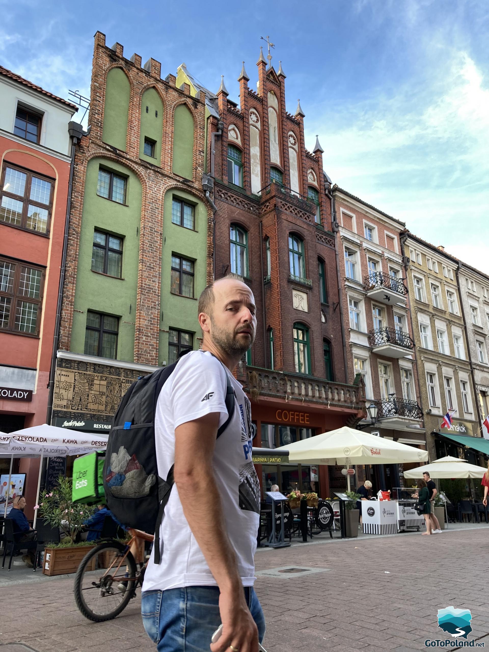 a man is in the foreground, behind him there are colorful tenement houses