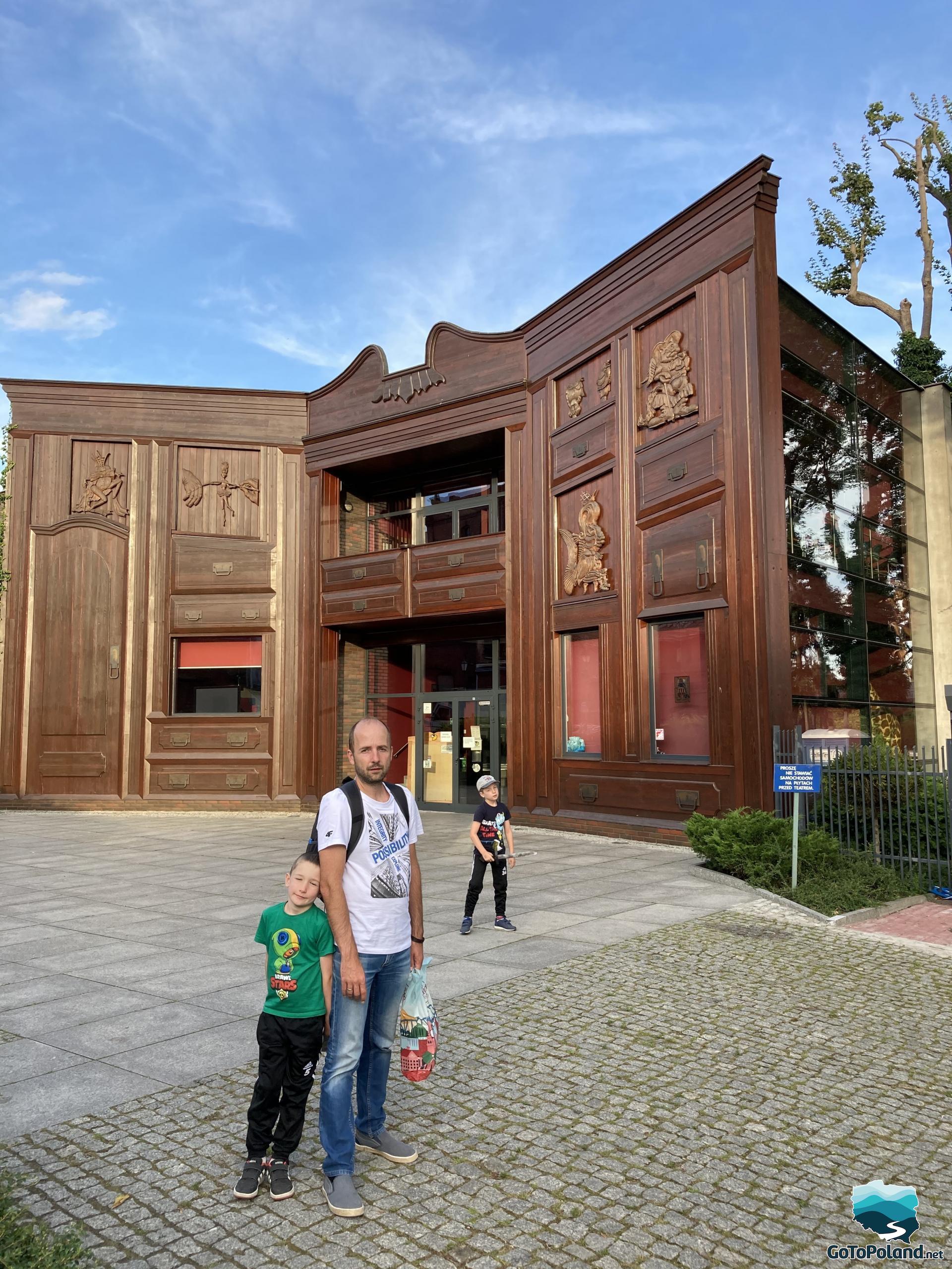 a man and two kids in front of a wooden building of the theatre