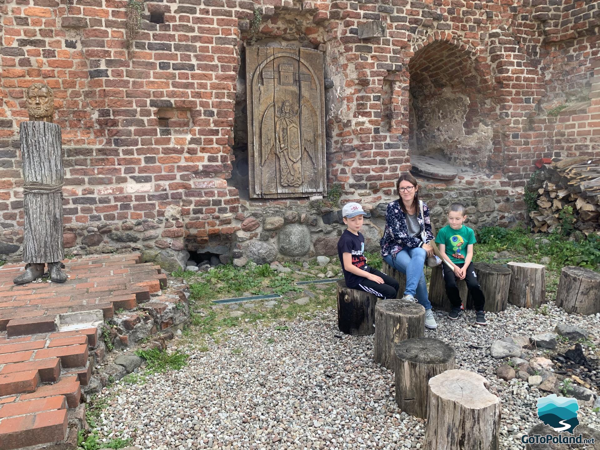 a woman and two children are sitting by the ruins of a castle on tree stumps