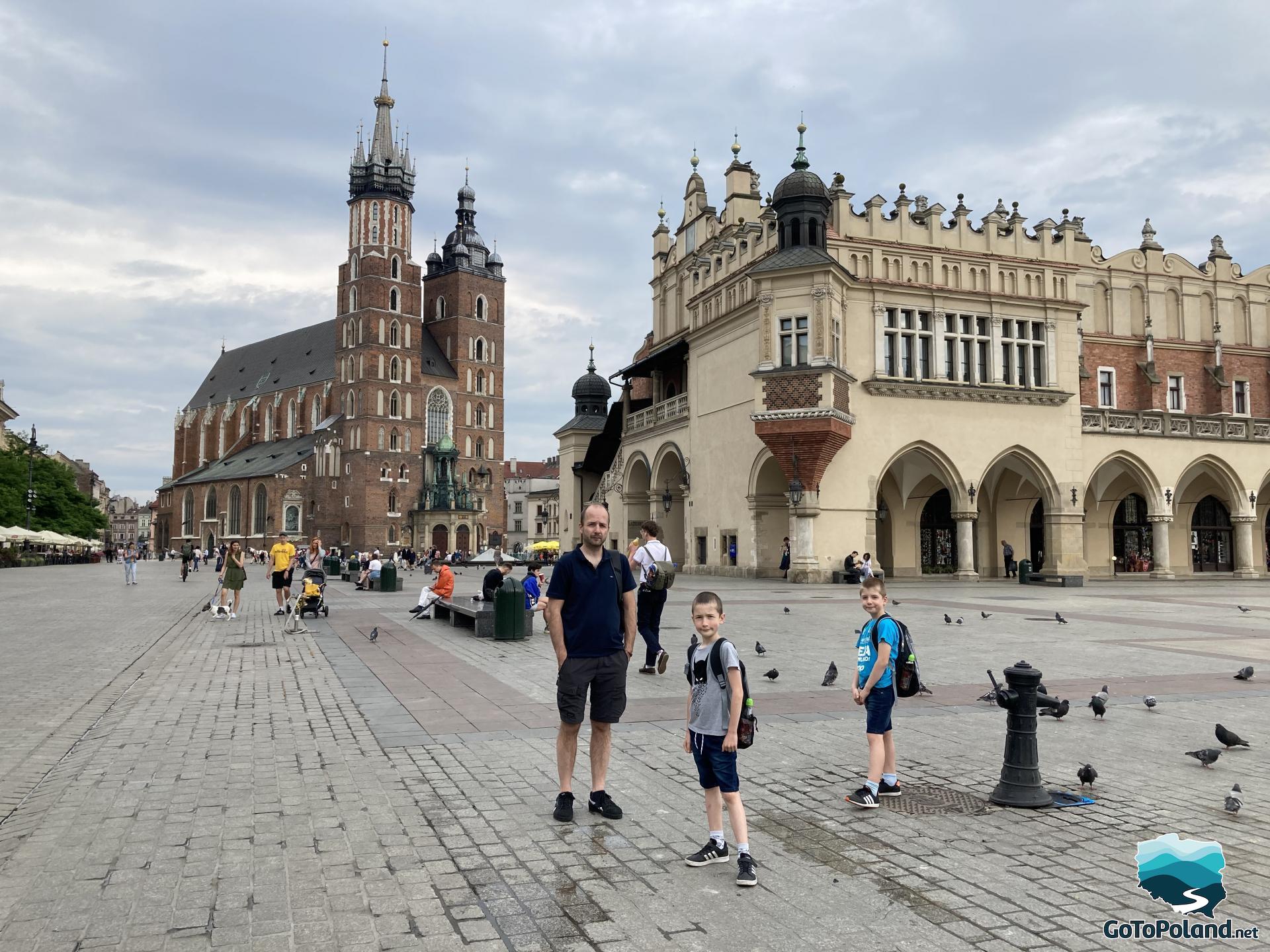a man and two children are standing in the Main Square, the Cloth Hall and a church in the background