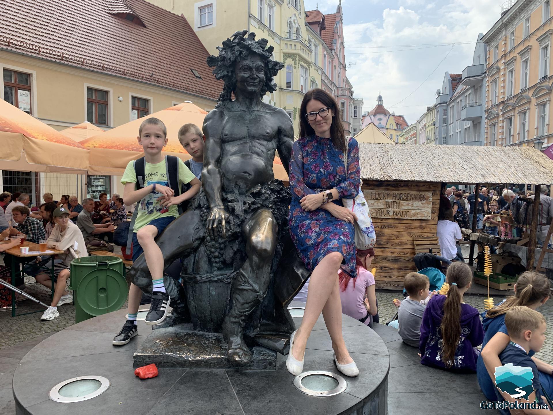 a woman and two children are sitting next to the Bacchus monument, a lot of tourists in the background