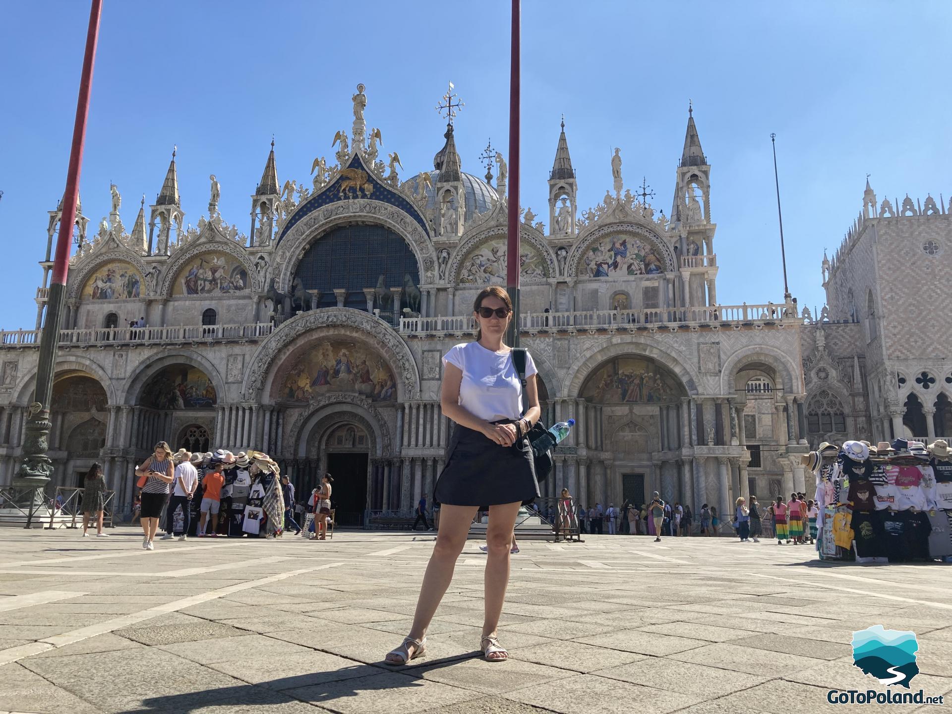 a woman is standing in front of Saint Marks Basilica, a magnificent church in Venice