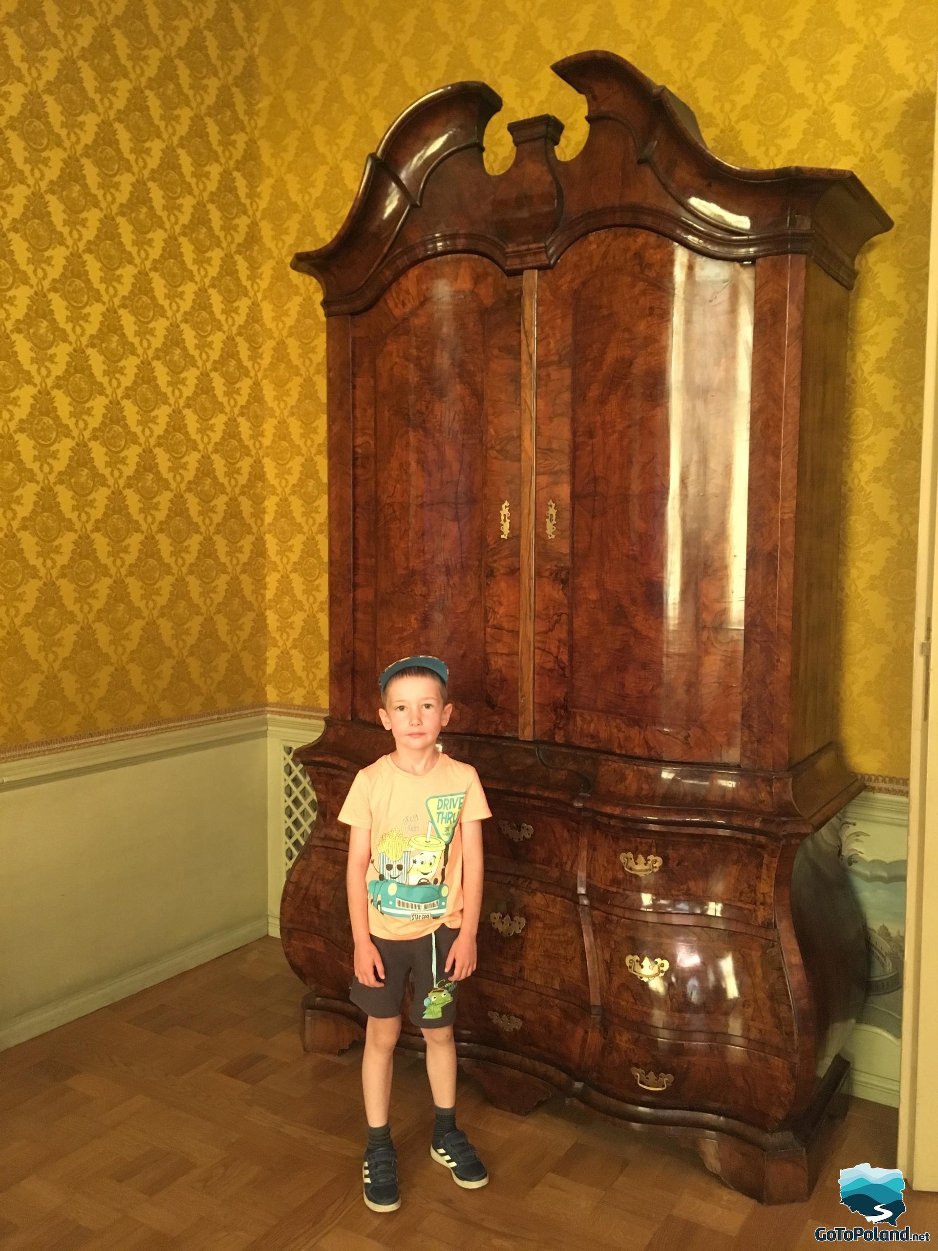 a young boy is standing in front of a large, old wardrobe
