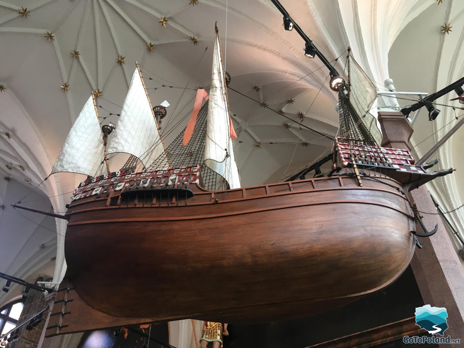 a model of a dark brown wooden ship with three white sails close up