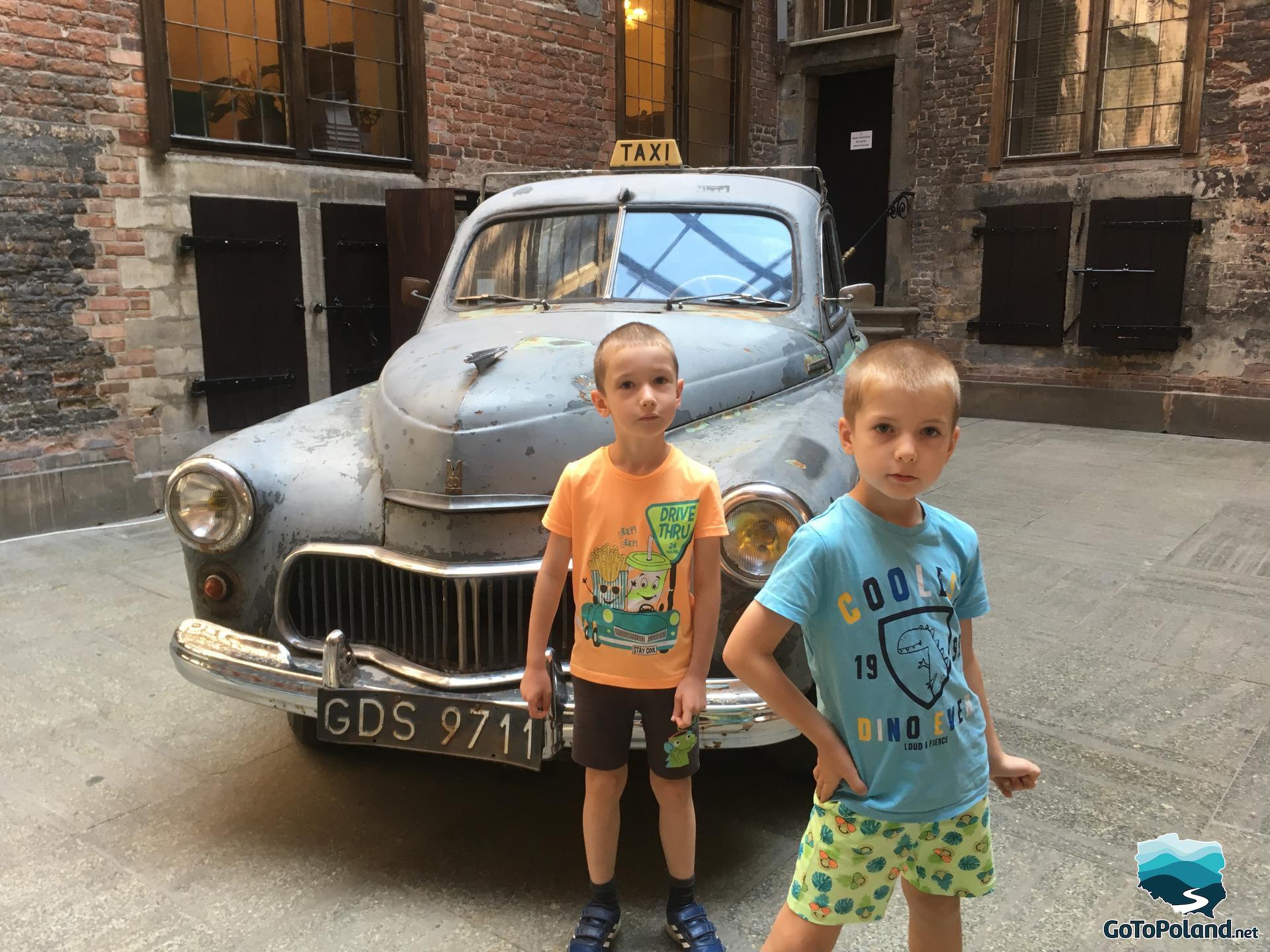 an old polish car called Warsaw is on an exhibition, two children in front of the car