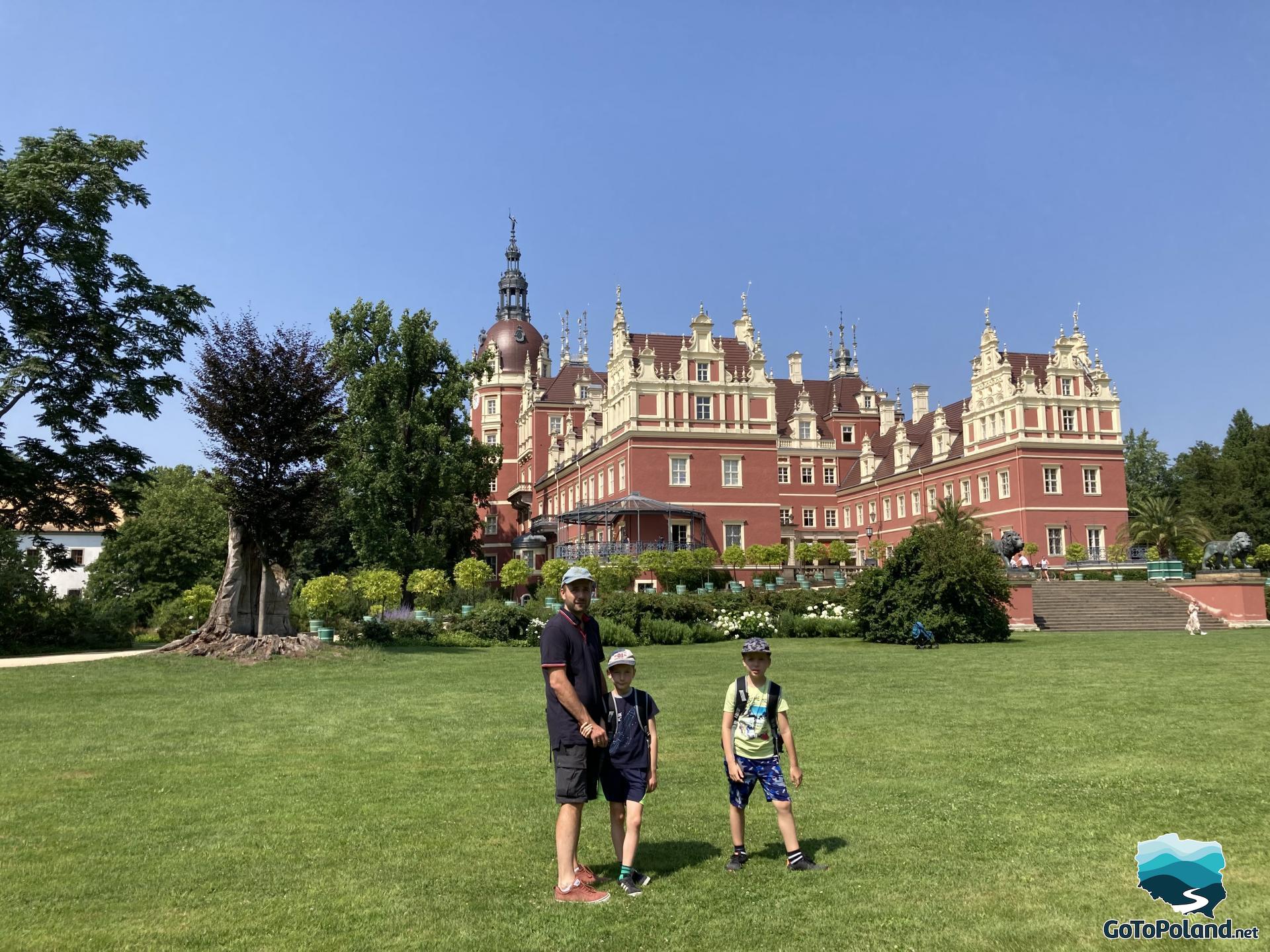 a red castle, a man and two boys are in front of it