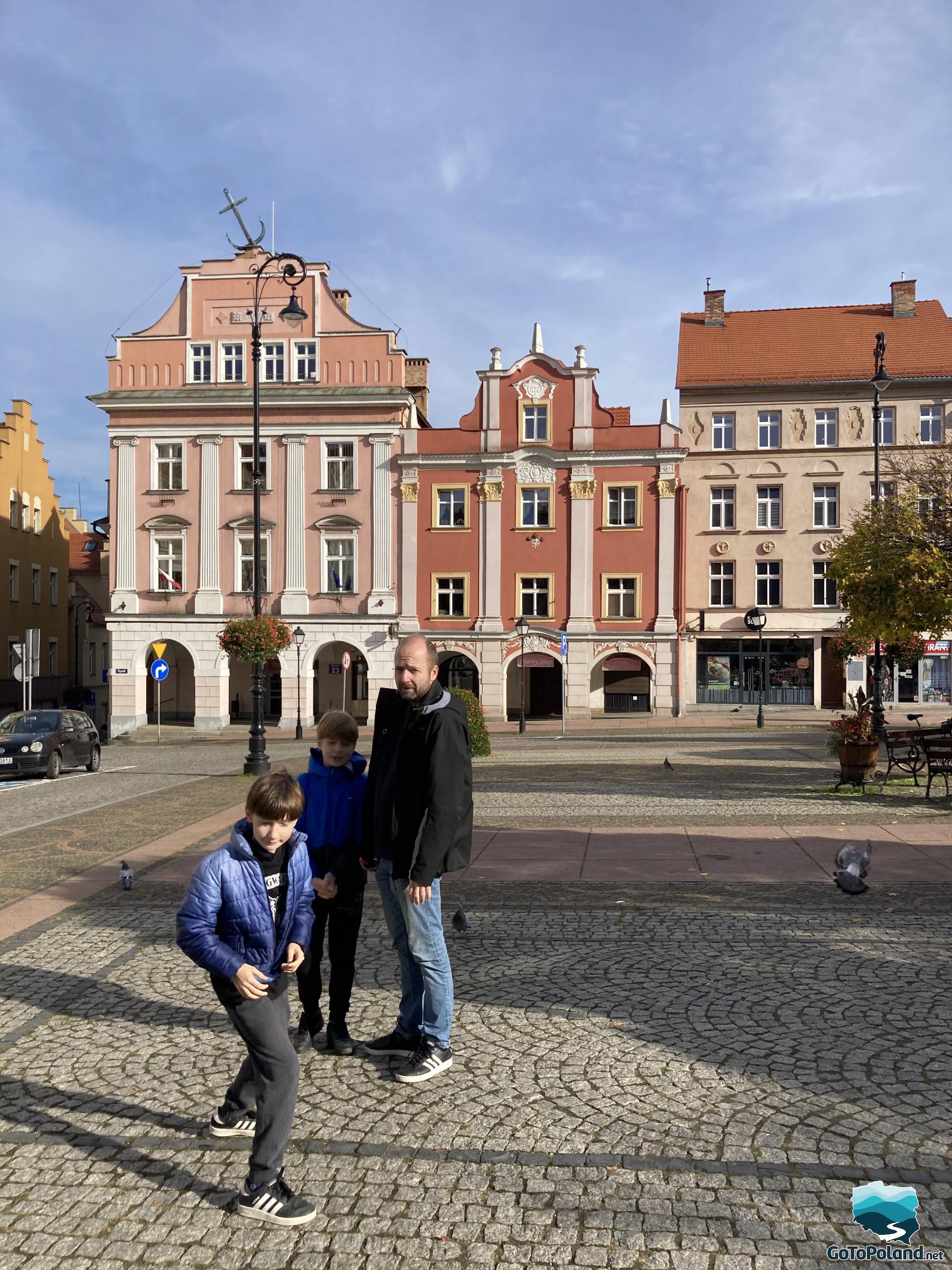 two children and a man are standing in the middle of the market square, several tenement houses behind them 