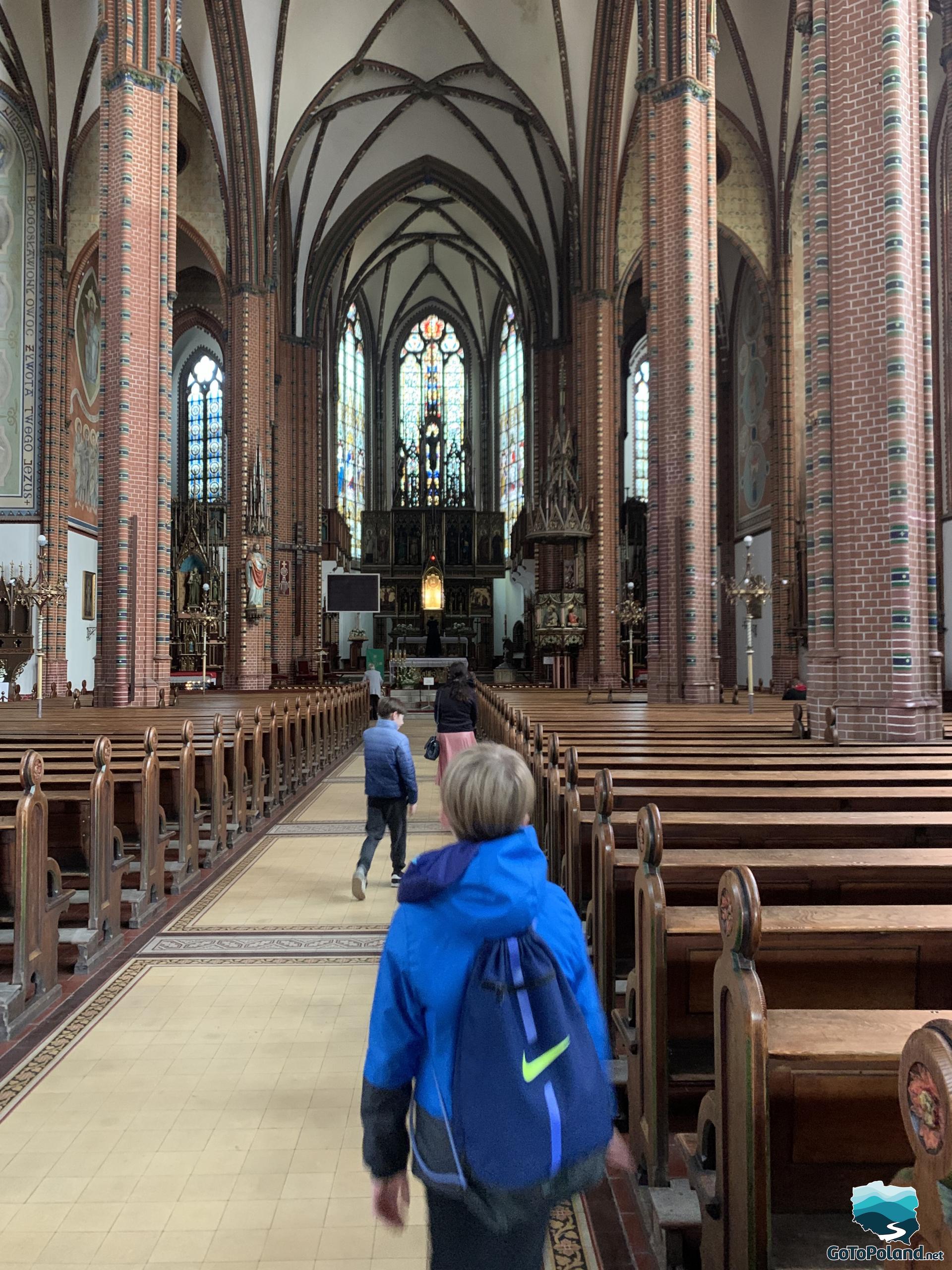 rows of pews in the church, very high brick pillars, altar in the background 