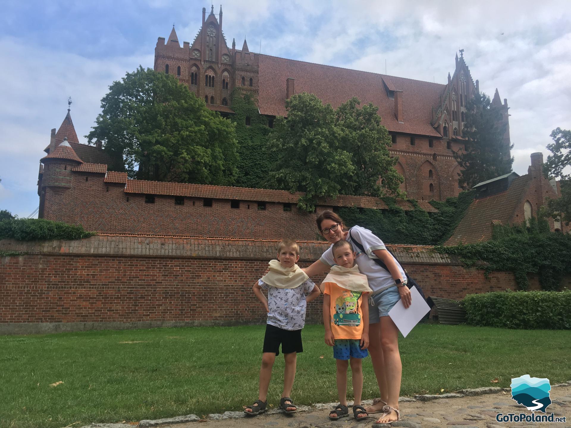 a woman and two boys are standing in front of the brick castle