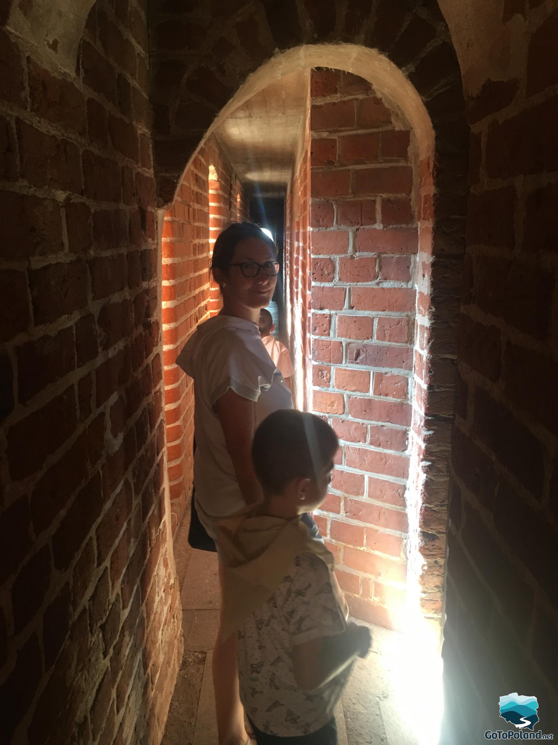 a woman and a boy are in a narrow passage in the castle