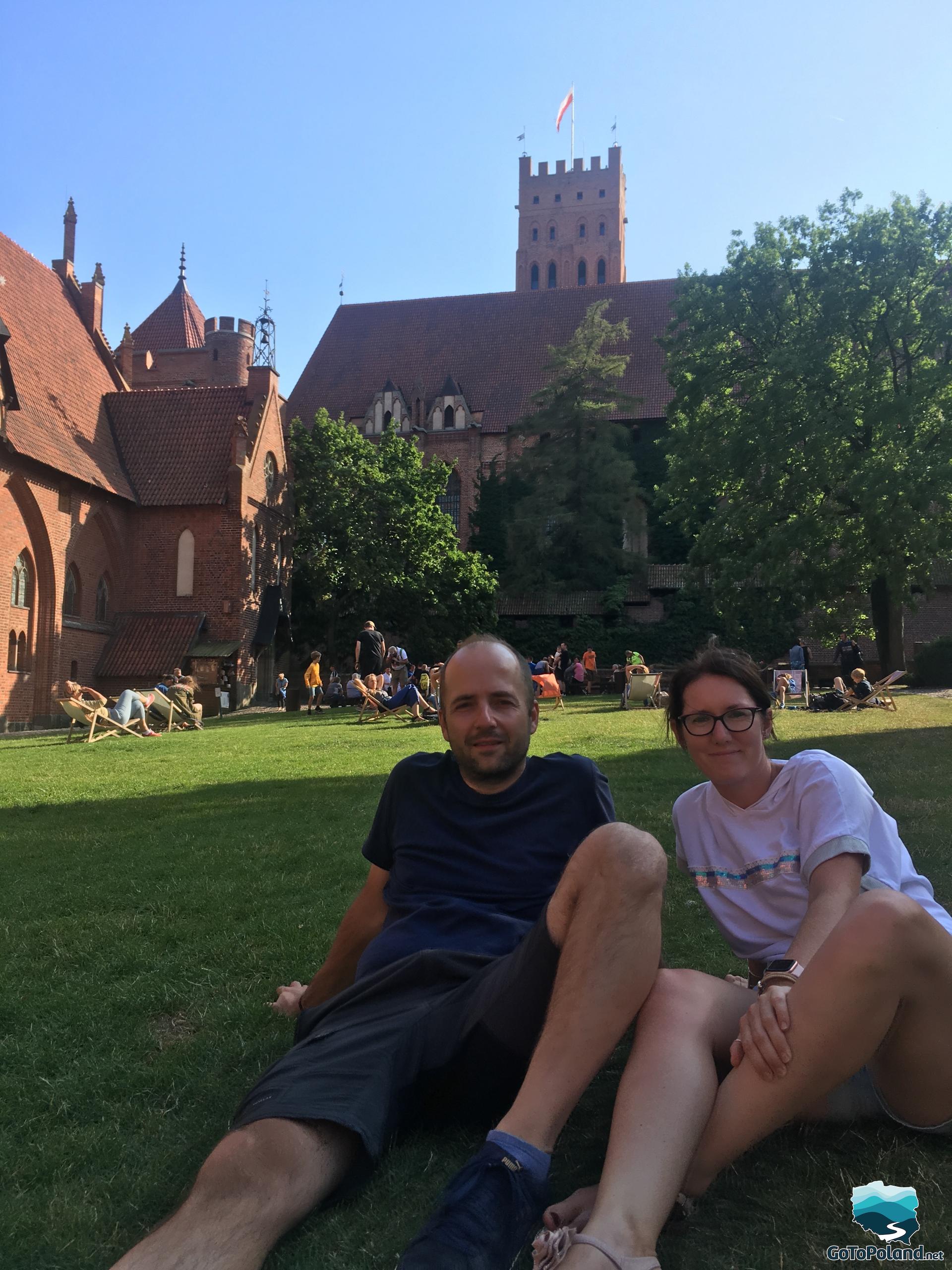 A woman and a man are sitting on the grass in the courtyard of the castle