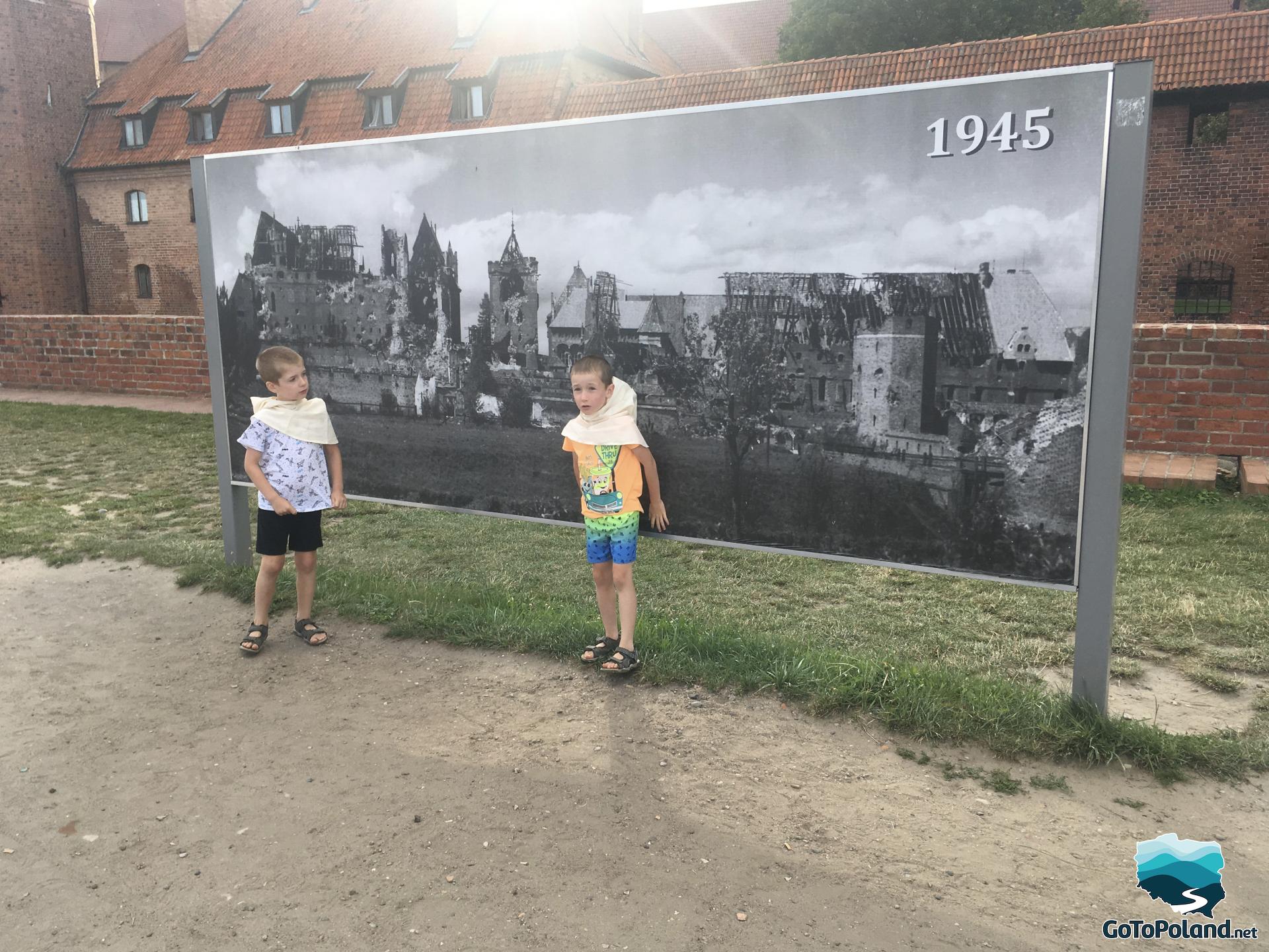 two boys are standing by a board which shows destroyed castle