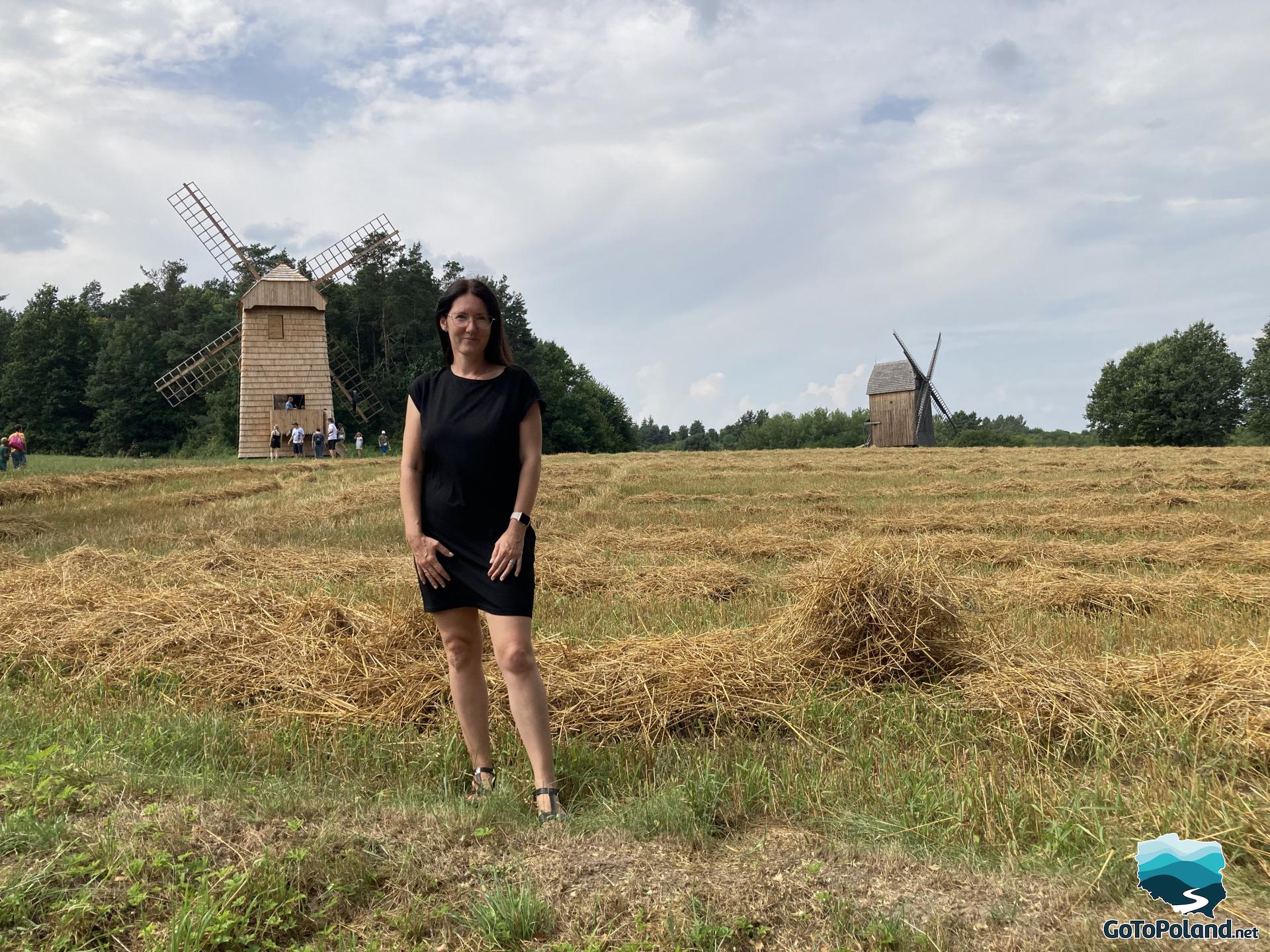 a woman is standing in a hay, behind her there are windmills 