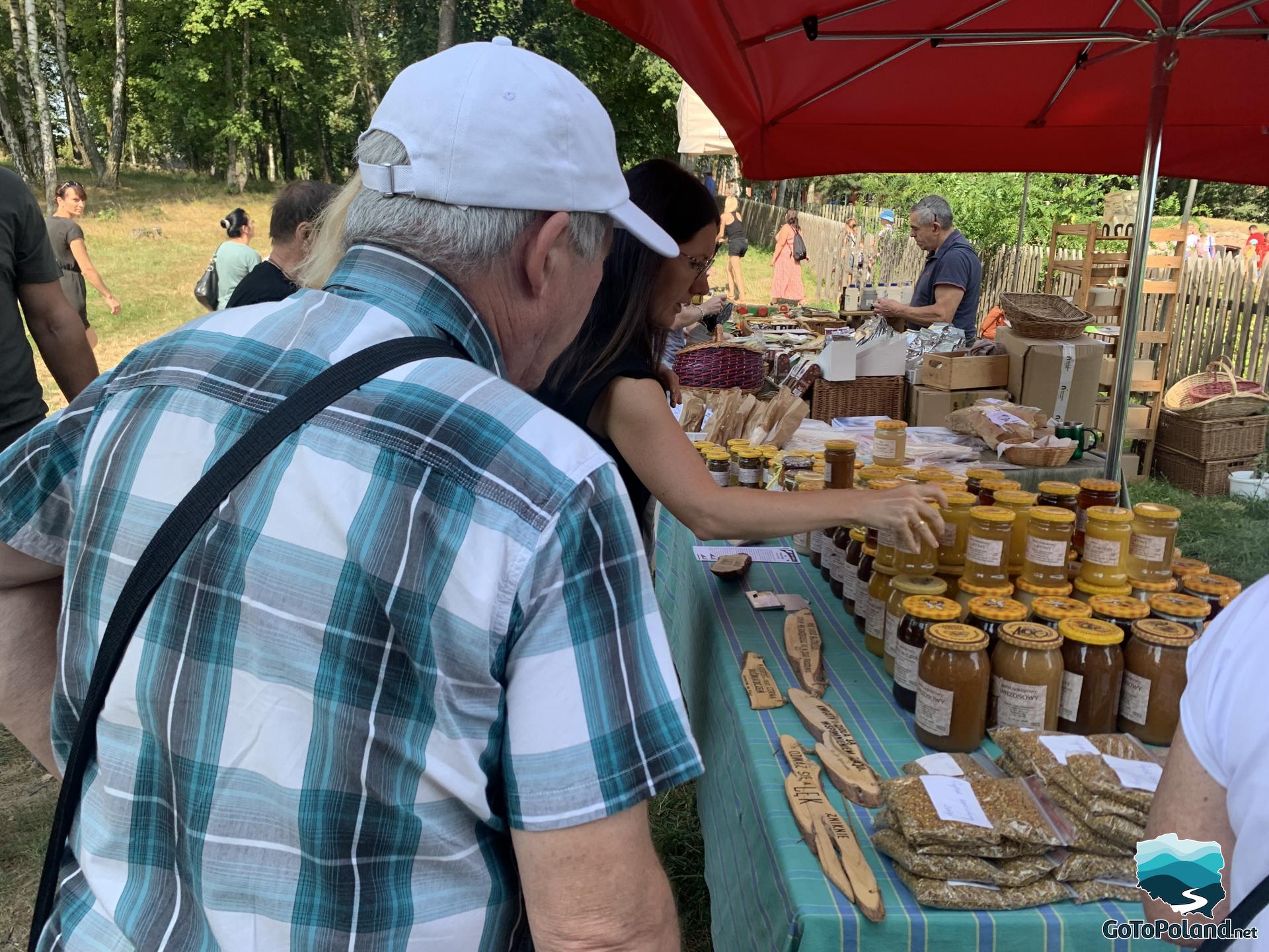 people watching products like jars of honey standing on a stall