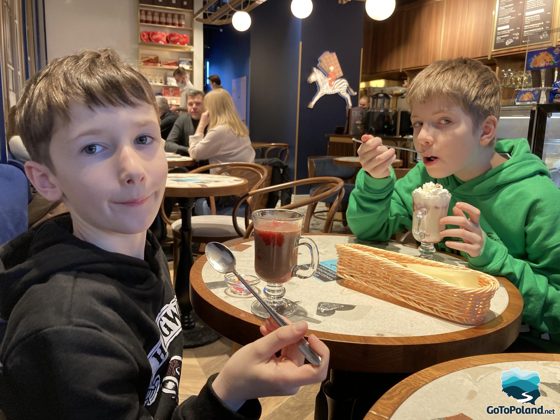 two boys sitting at a table in a cafe and drinking hot chocolate